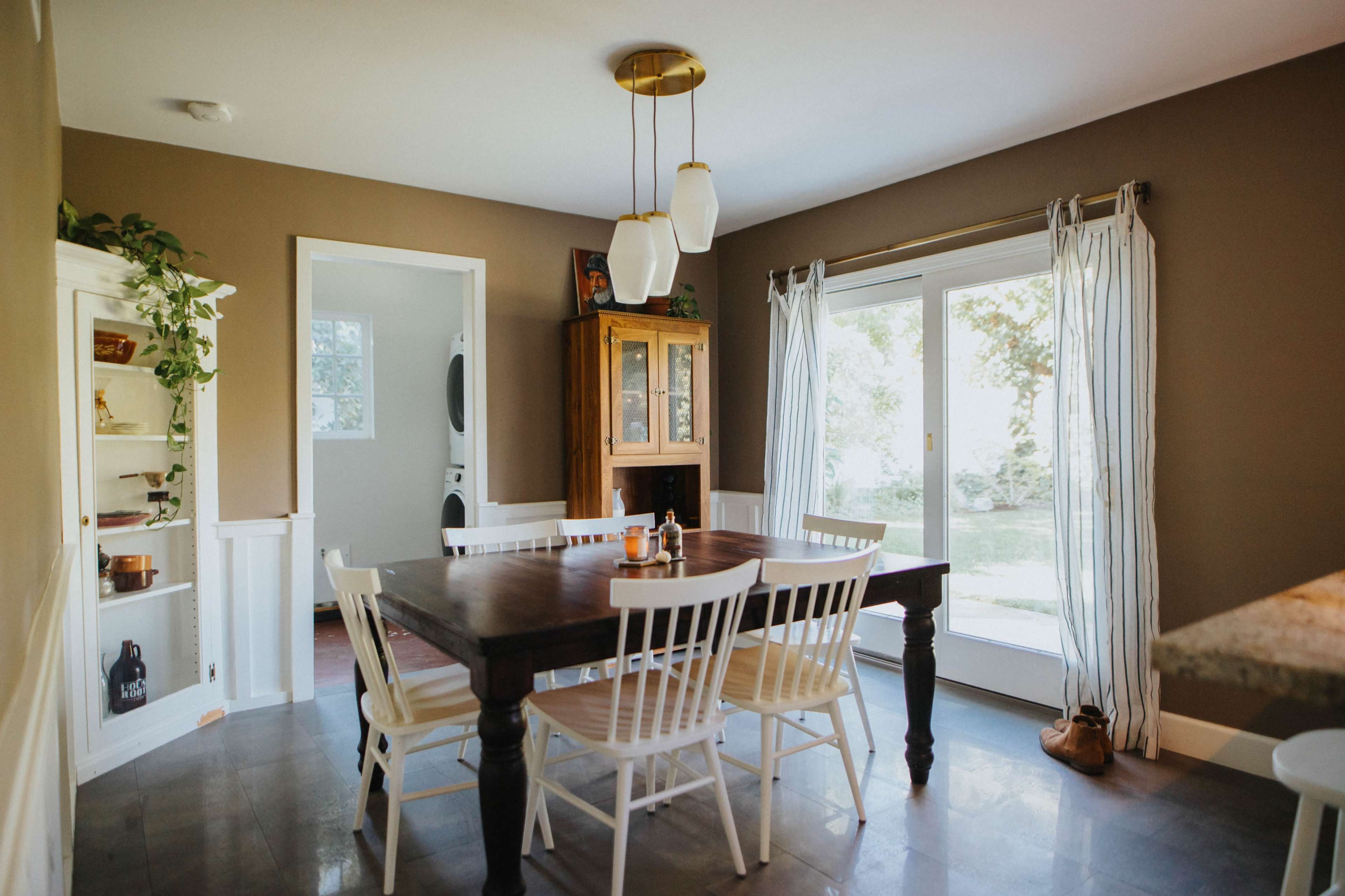 A dining area features a wooden table surrounded by white chairs, with a large window and door that offers views of the outdoors.