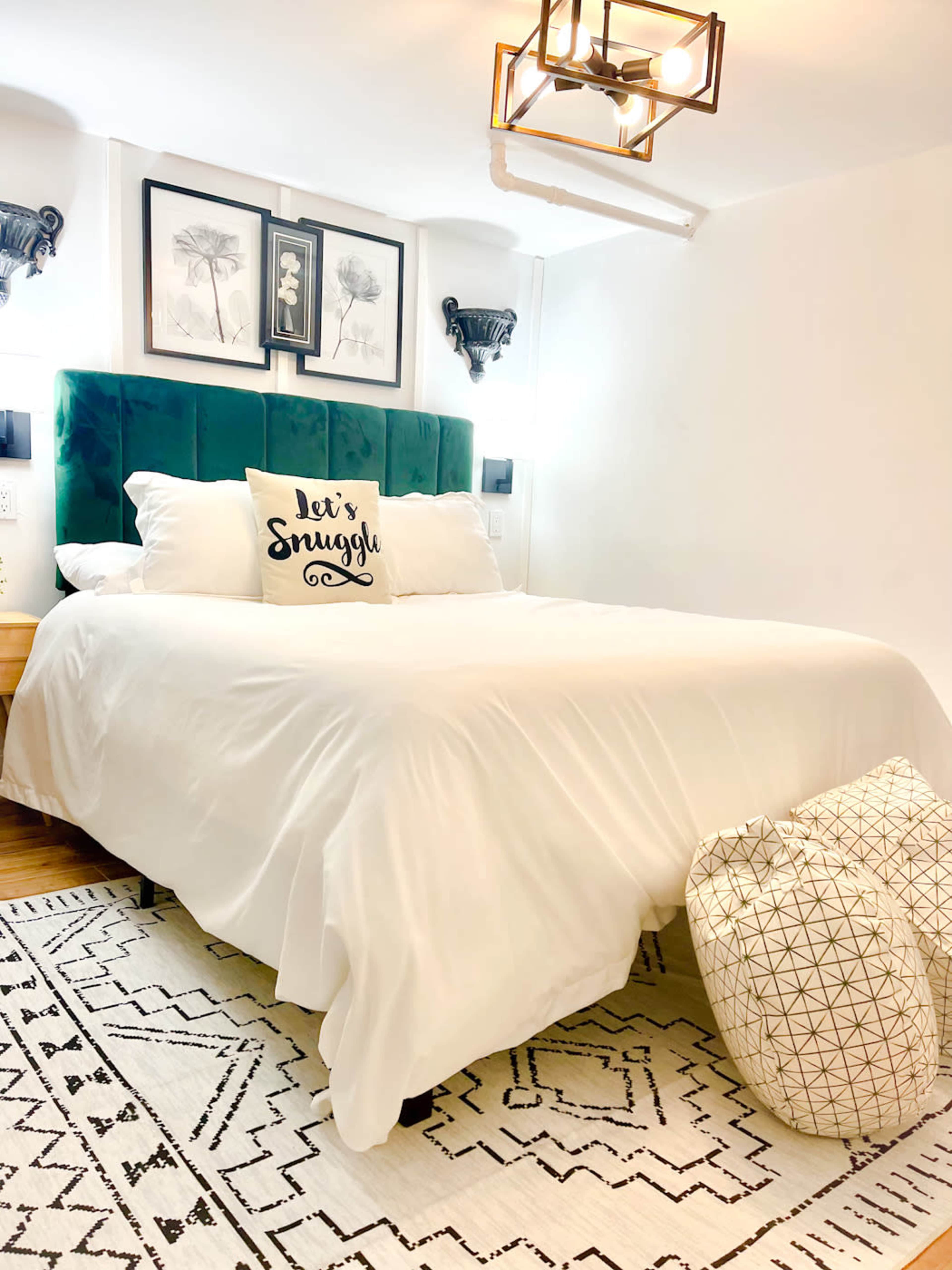 A neatly made bed with a white comforter, adorned with decorative pillows, and a geometric patterned rug on the floor.