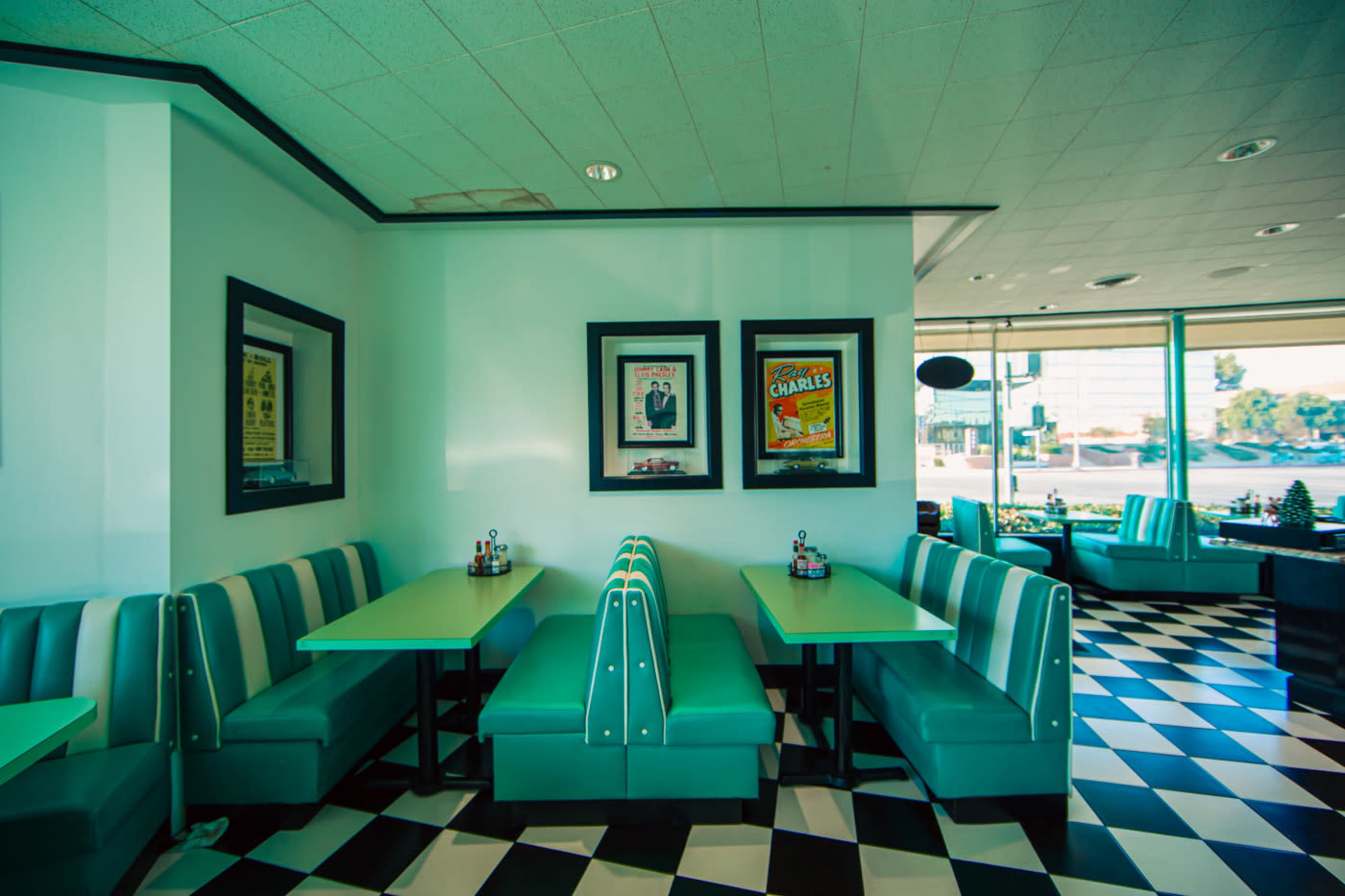 The image shows a brightly colored diner interior featuring teal booths, black and white checkered tiles, and framed vintage posters on the walls.