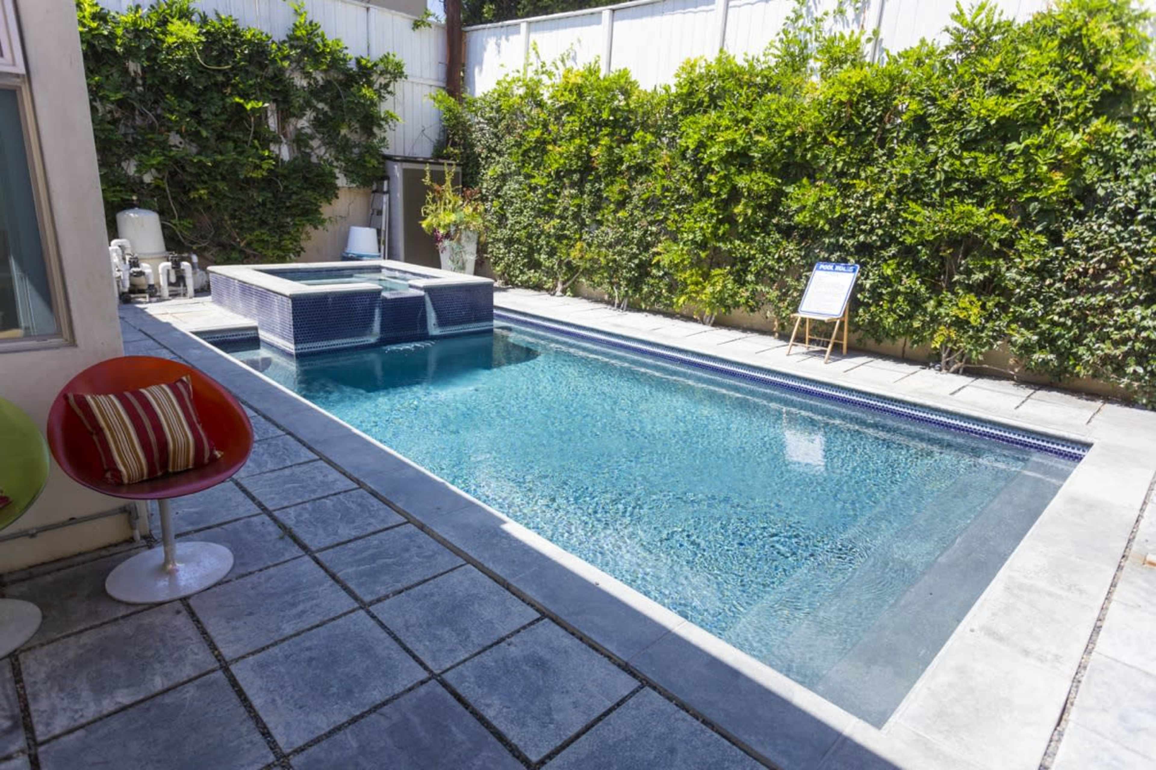 A rectangular swimming pool with a spa on one end, surrounded by a concrete patio and lush greenery.