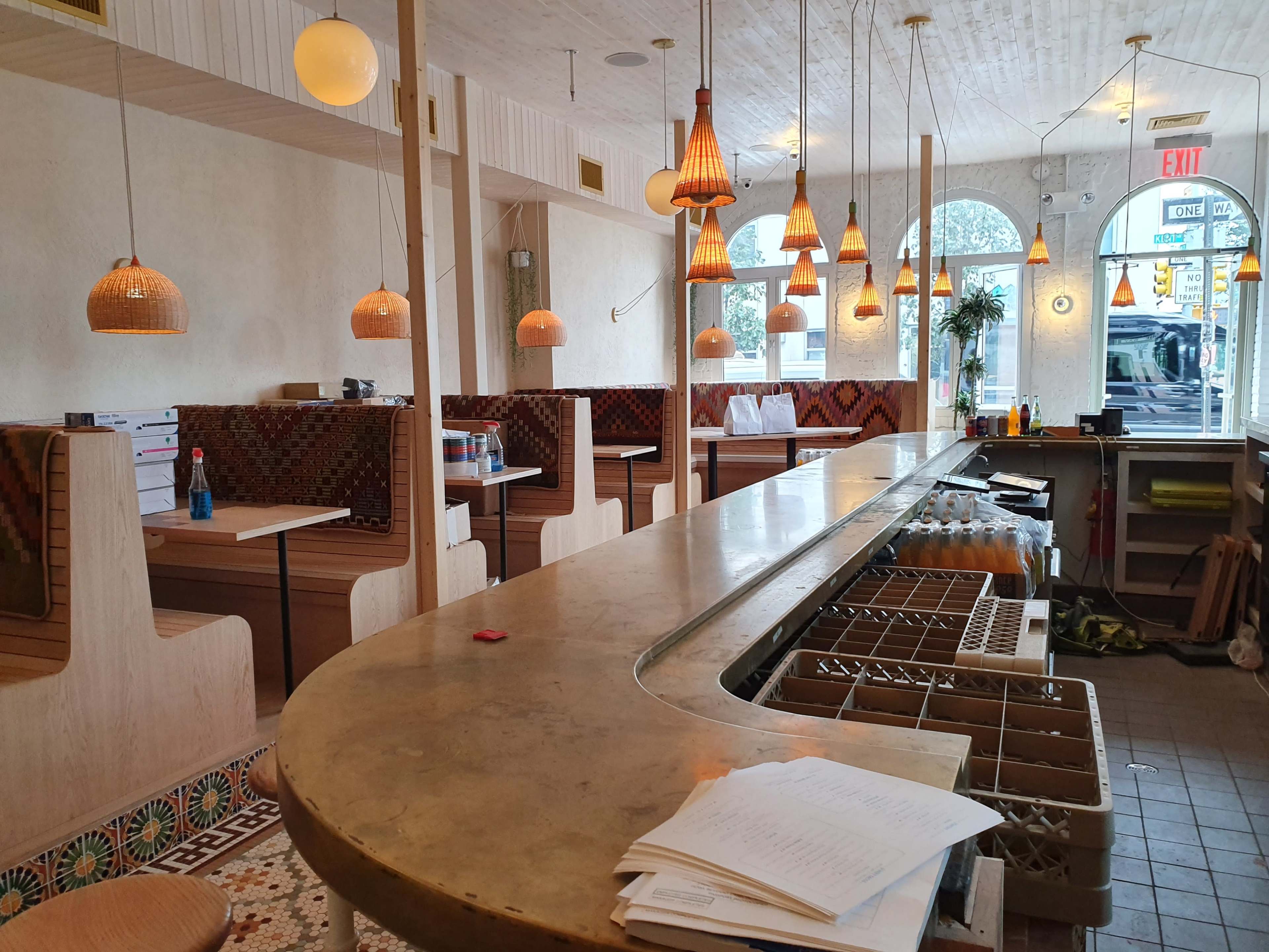 A modern restaurant interior with a curved bar, wooden booths, and decorative pendant lighting.