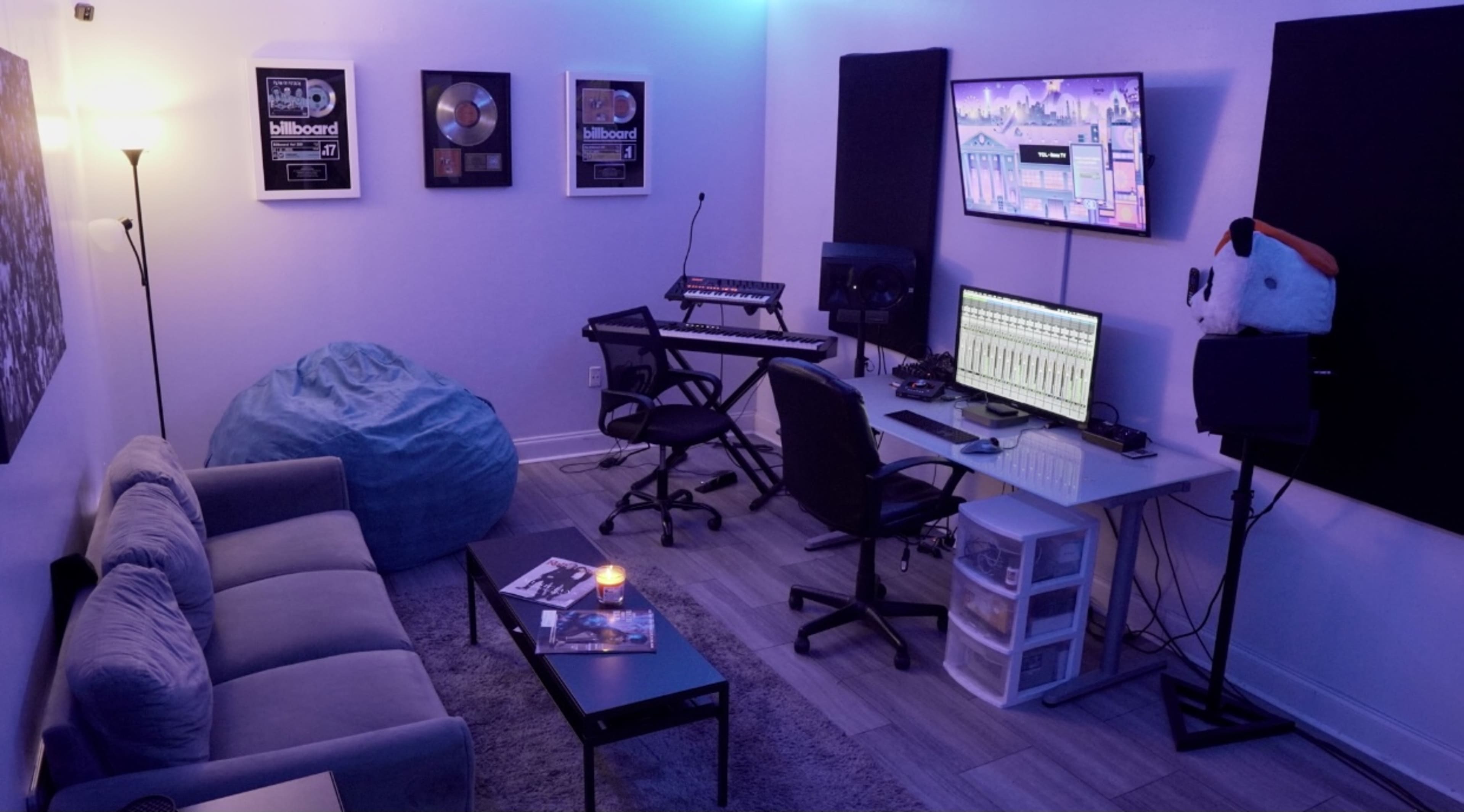 The image shows a music production studio with a sofa, a table with equipment, a computer setup, and ambient lighting.
