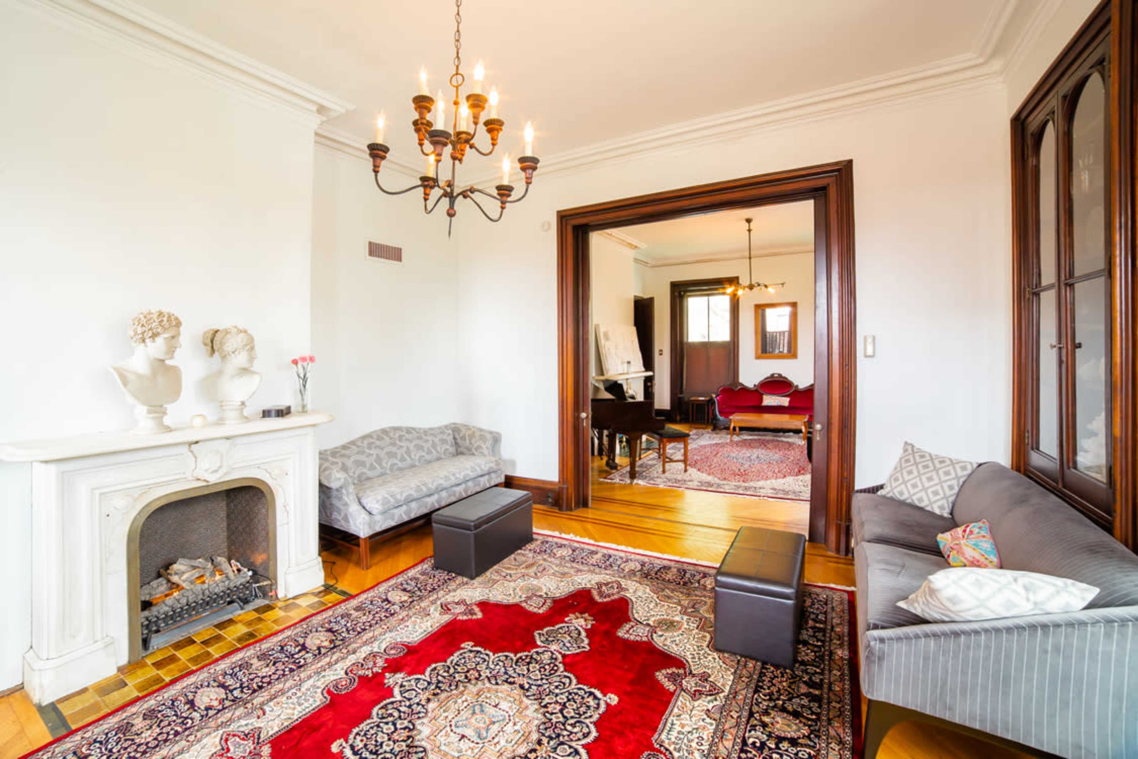 A living room with a fireplace, two sofas, a chandelier, and an archway leading to another room furnished with chairs and a decorative rug.