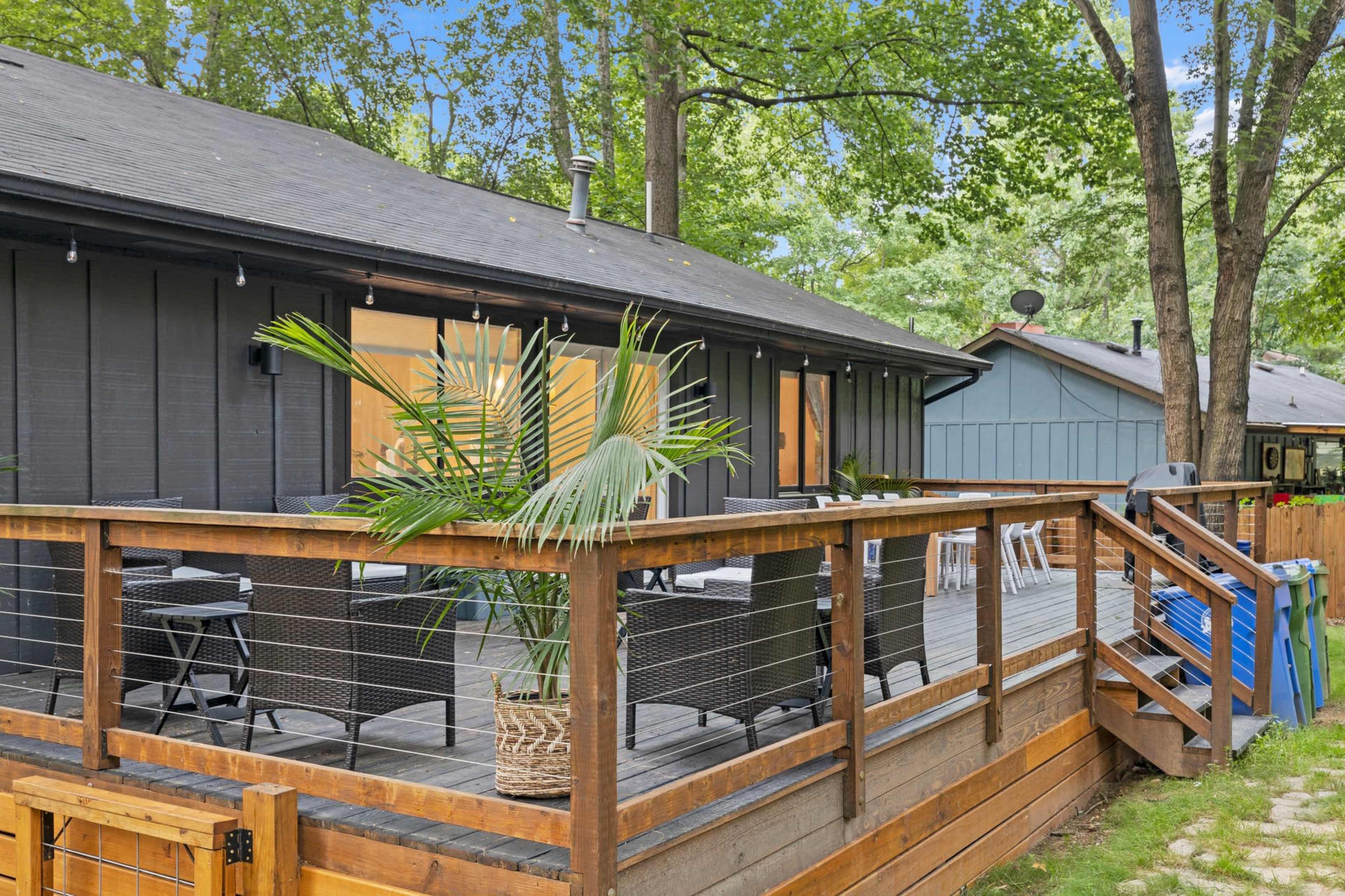 A wooden deck with seating overlooks a yard surrounded by trees.