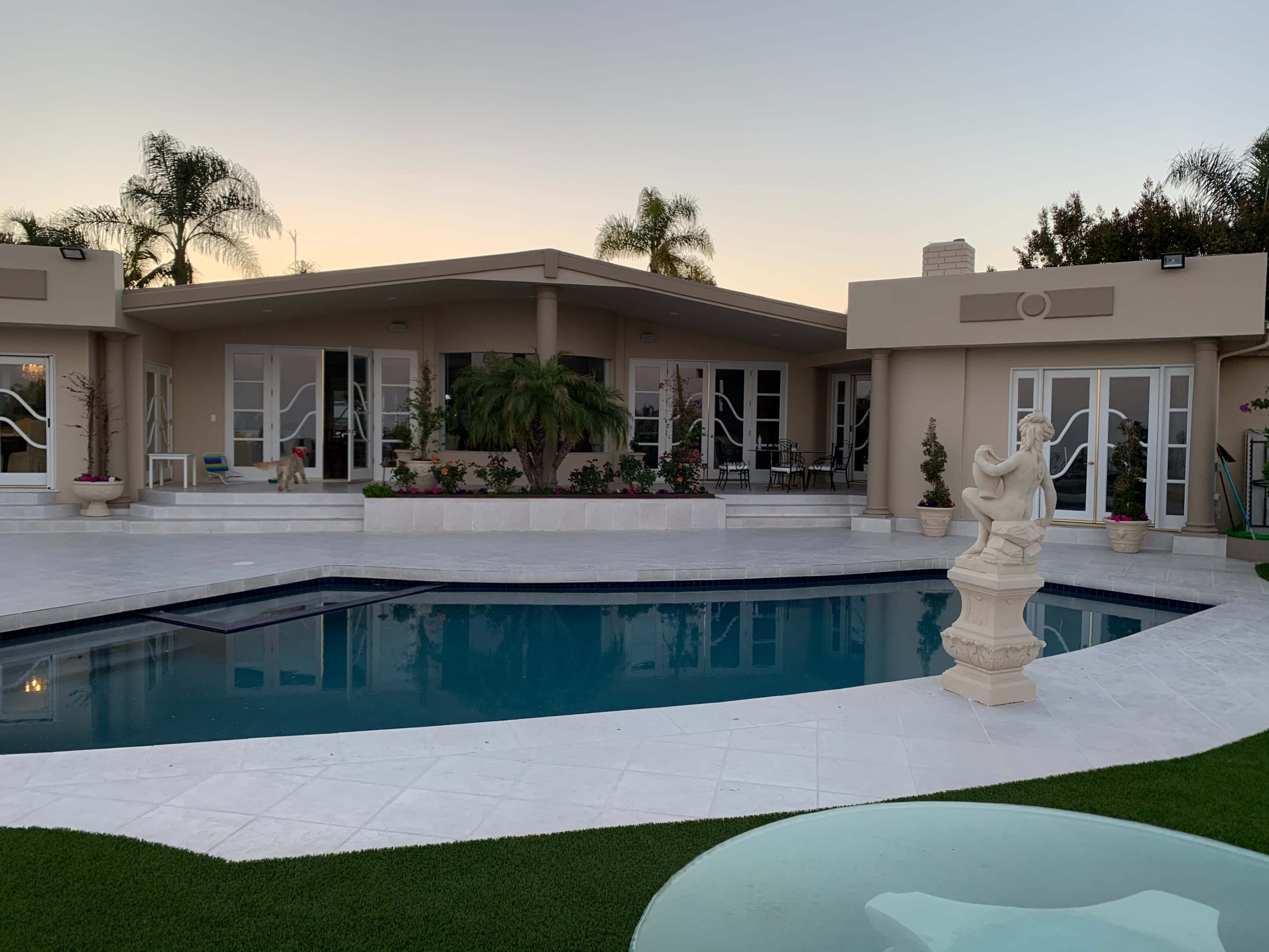 A modern house with a pool surrounded by palm trees and landscaped gardens.