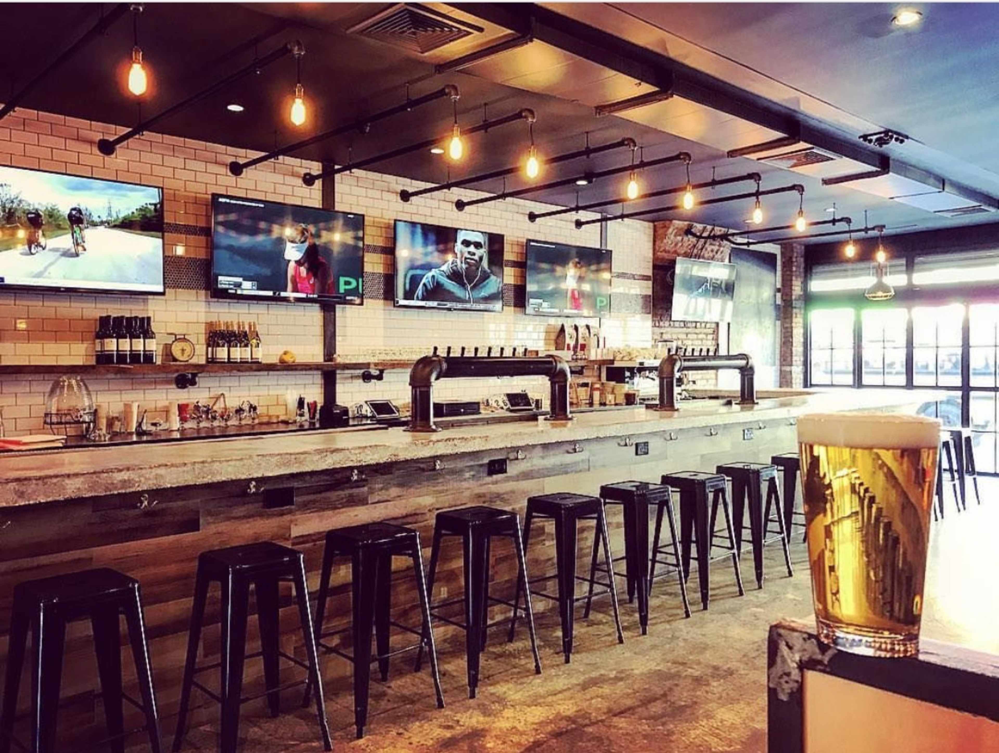 A bar with a concrete countertop, several bar stools, and multiple television screens displaying various sports events.