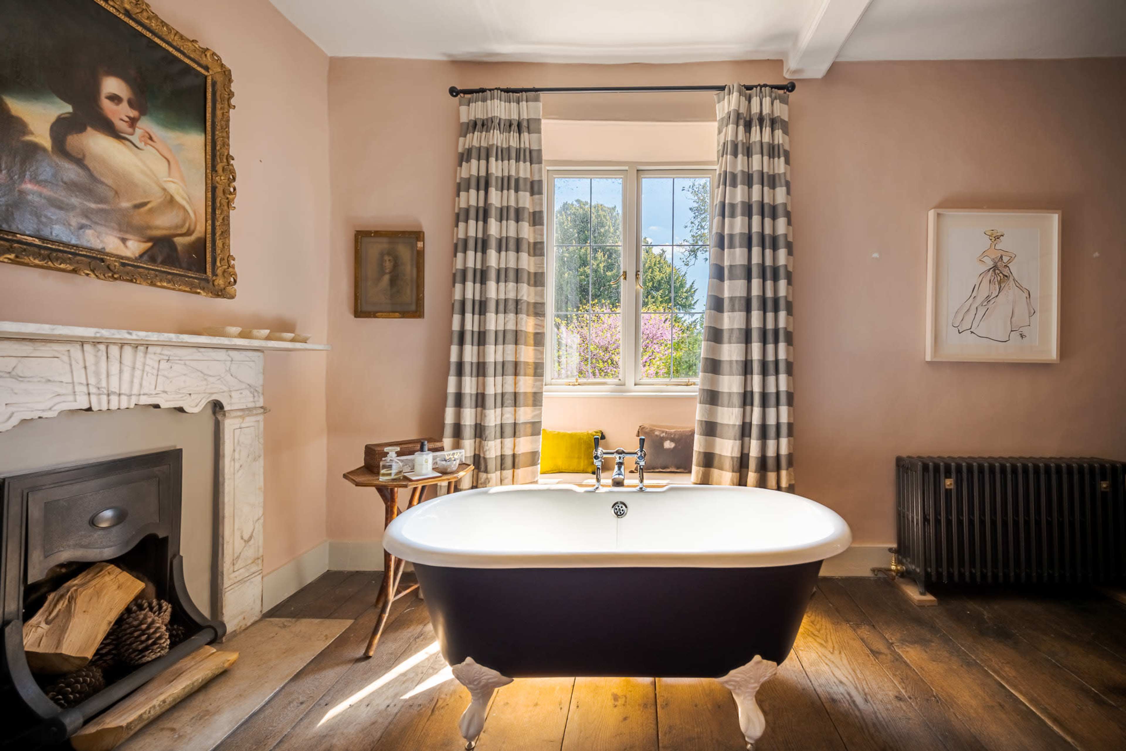 The image shows a stylish bathroom featuring a freestanding bathtub, a fireplace with a marble mantel, and large windows with patterned curtains that allow natural light to illuminate the space.
