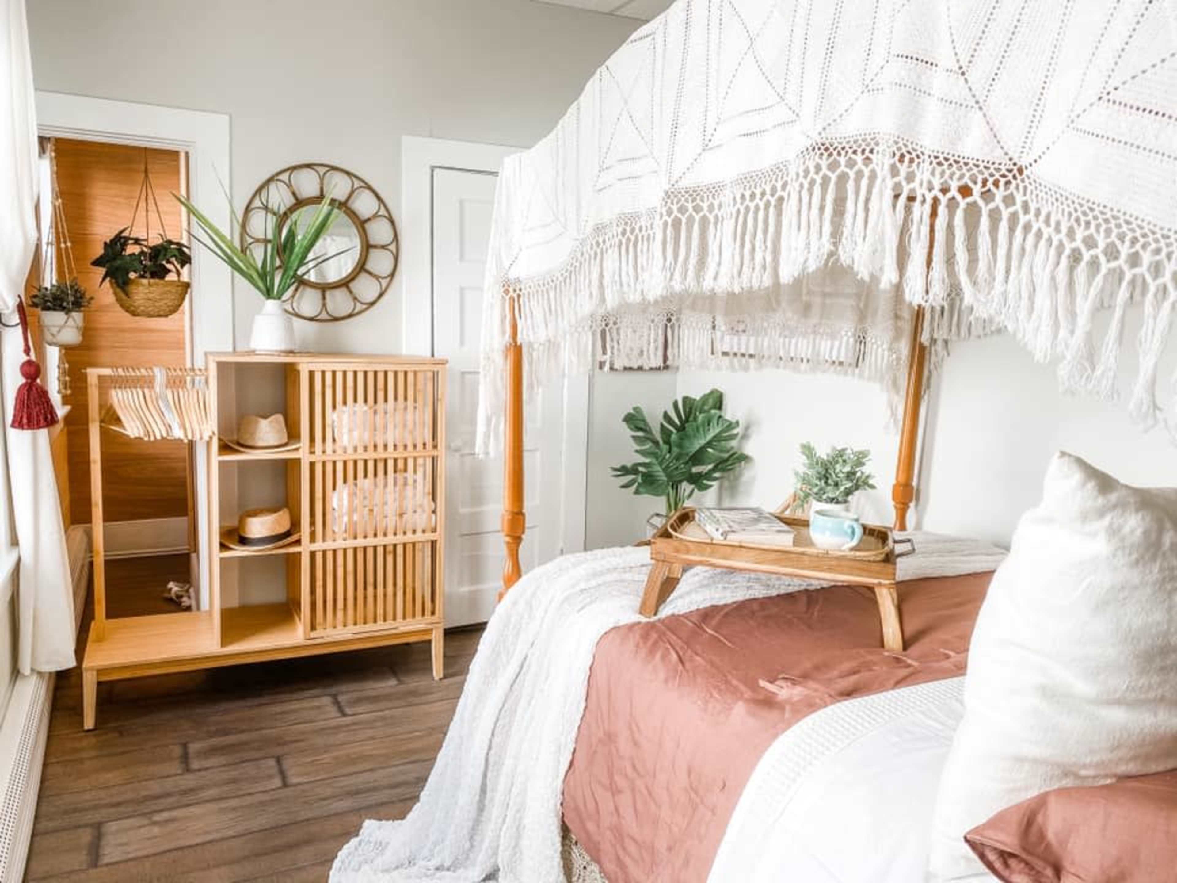 A cozy bedroom features a bed with a canopy draped in intricate lace, accompanied by a wooden storage unit and potted plants.
