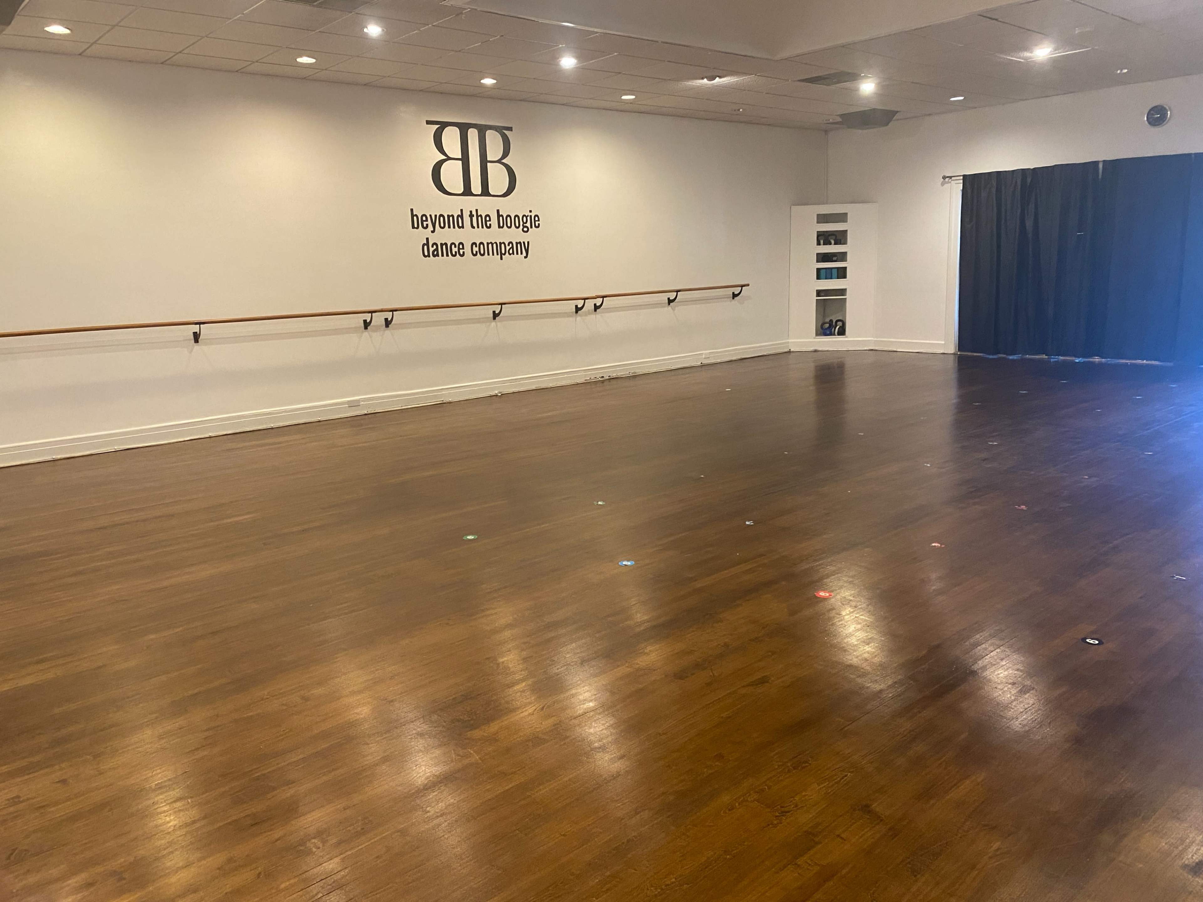 A spacious dance studio with a polished wooden floor and a wall displaying the logo of "Beyond the Boogie Dance Company."