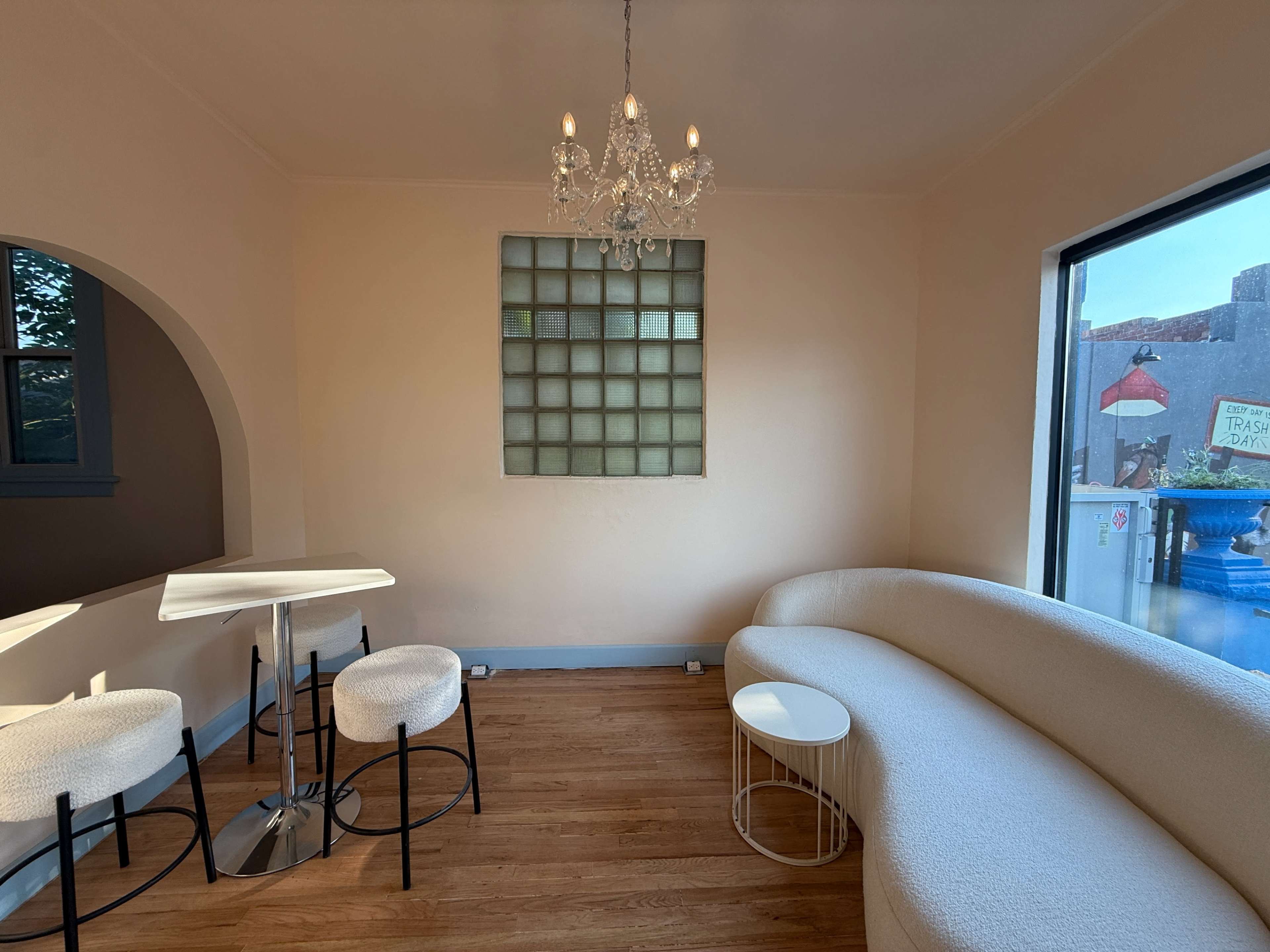 The image shows a modern, minimalist interior featuring a curved couch, a small round table, and a unique glass block window.