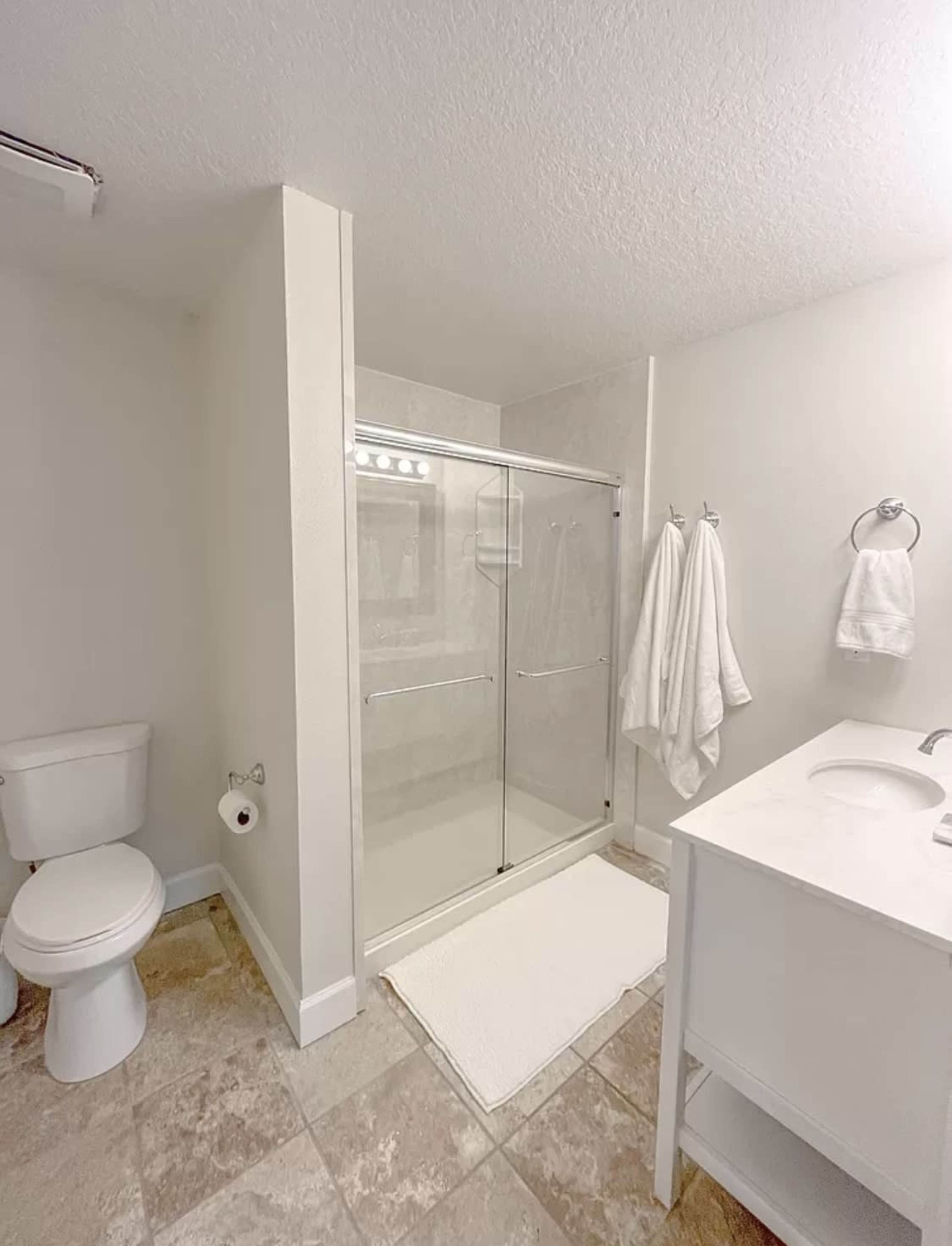 The image shows a modern bathroom featuring a glass shower enclosure, a white vanity with a sink, a toilet, and plush towels hanging on a rack.