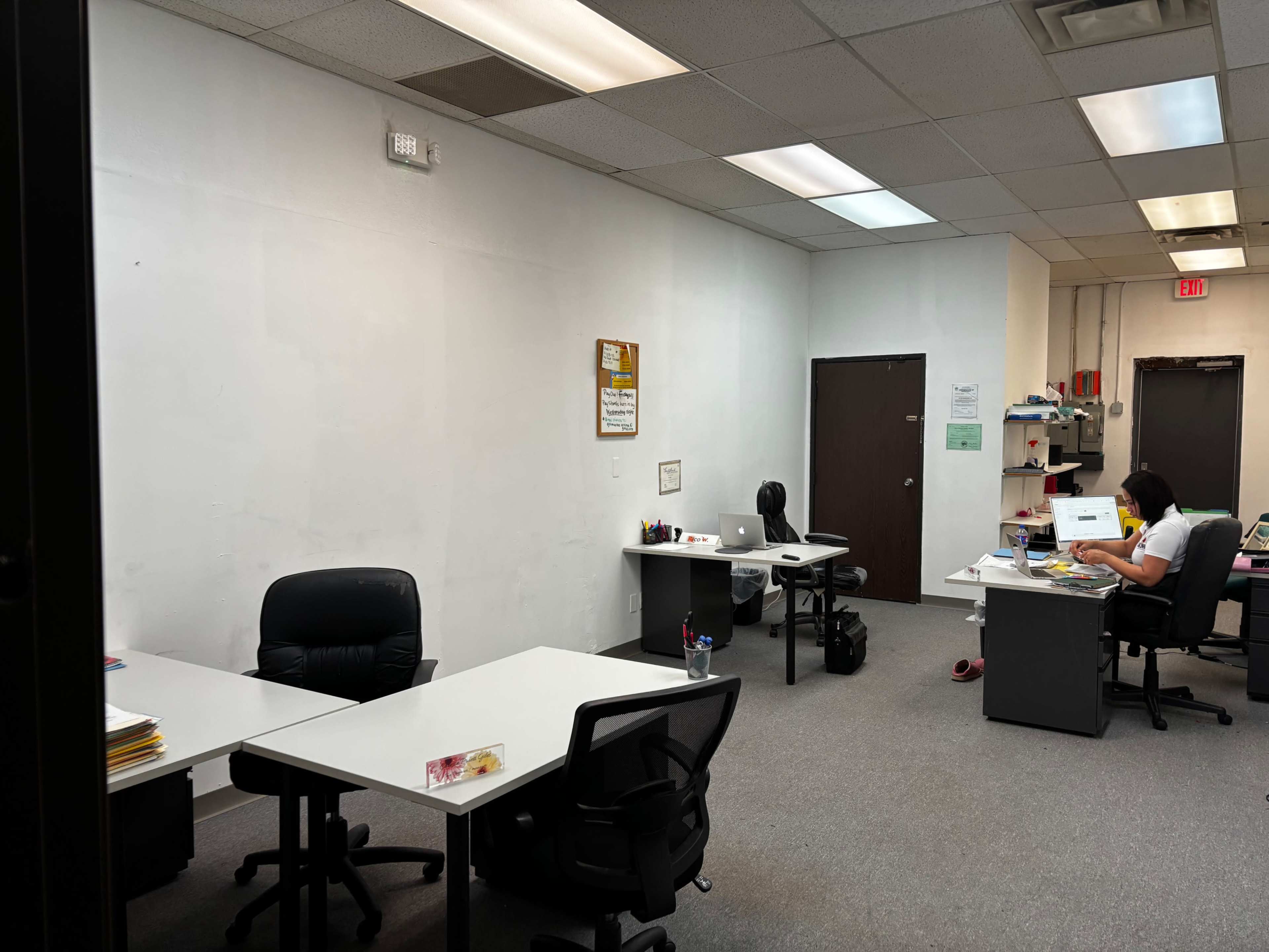 The image shows an office space with multiple desks, chairs, and a person working at a desk in the background.