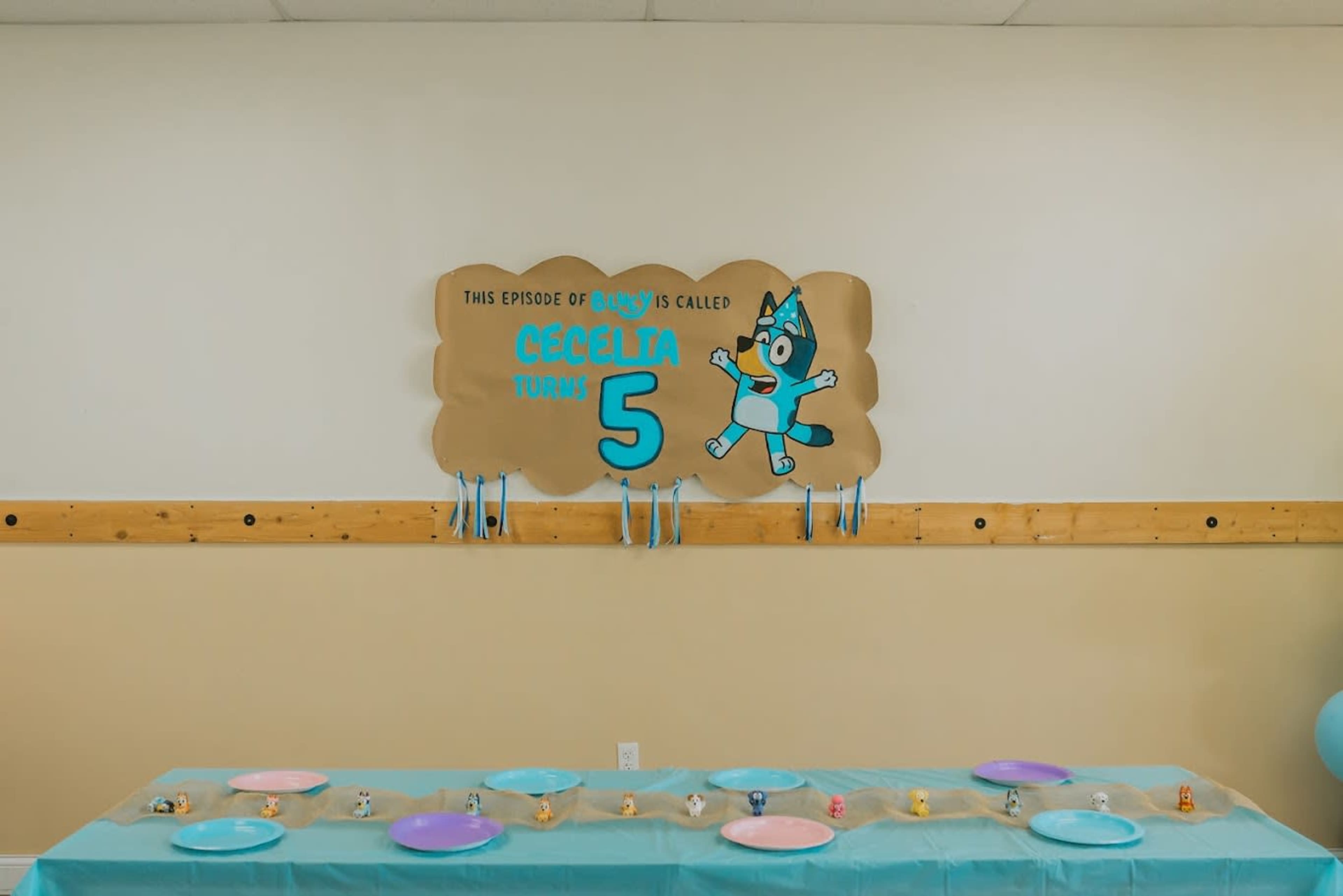 The image shows a birthday party setup with a sign that reads "Cecilia turns 5" and a long table decorated with colorful plates and party items.