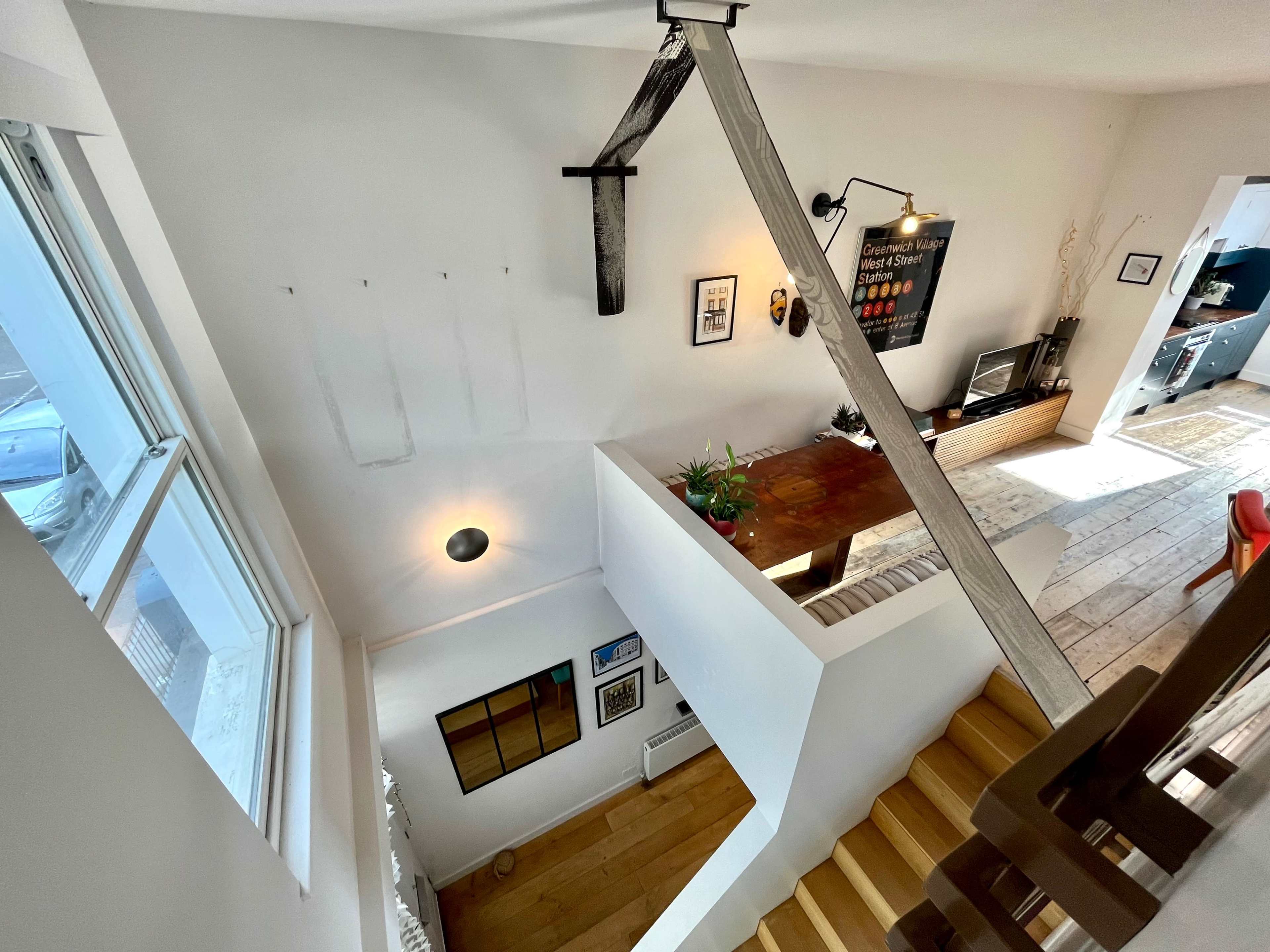 The image shows an interior space with a staircase leading down to a dining area, featuring a wooden table and wall-mounted decor.