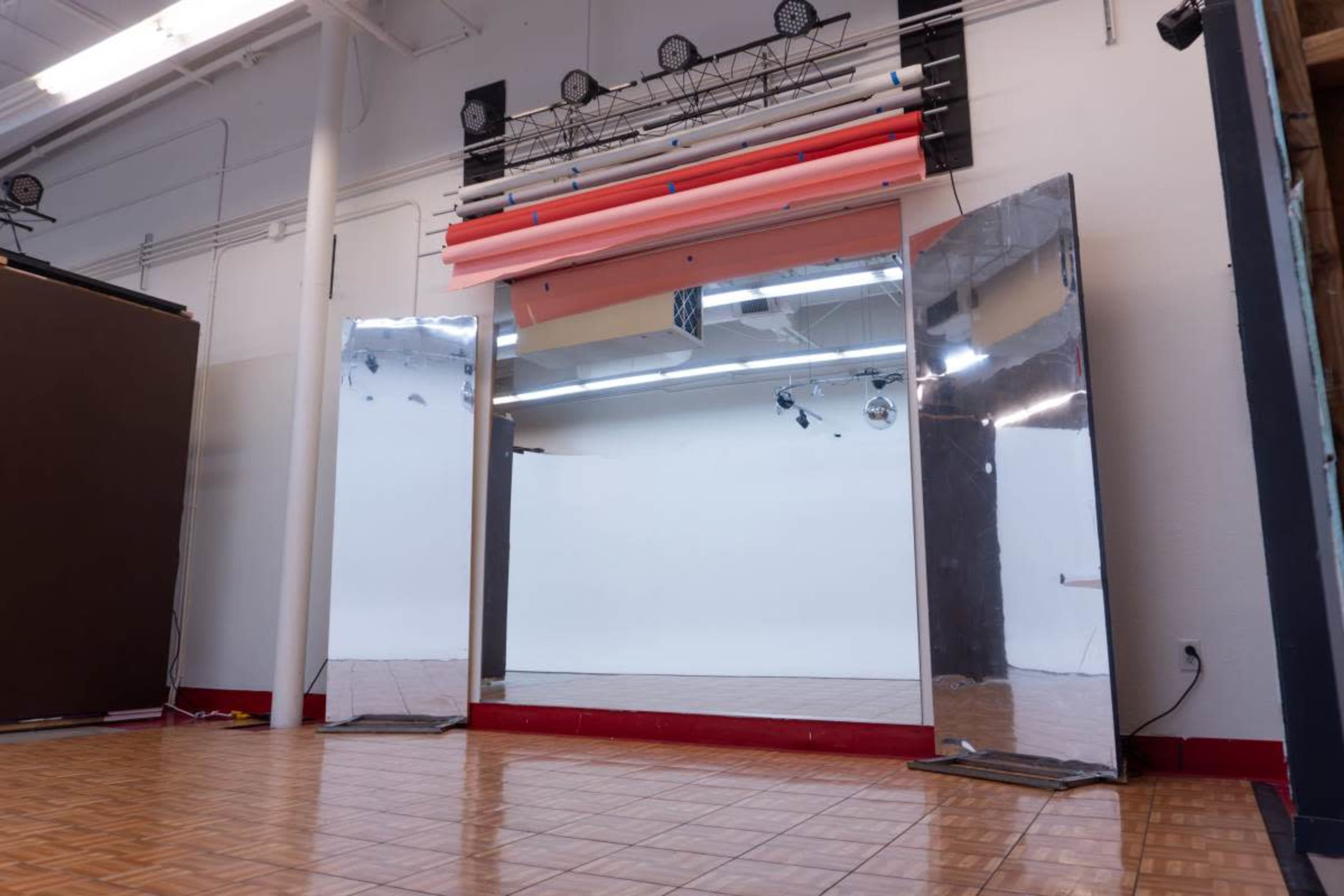 The image shows a spacious studio with large mirrors, a clean backdrop, and wooden flooring.