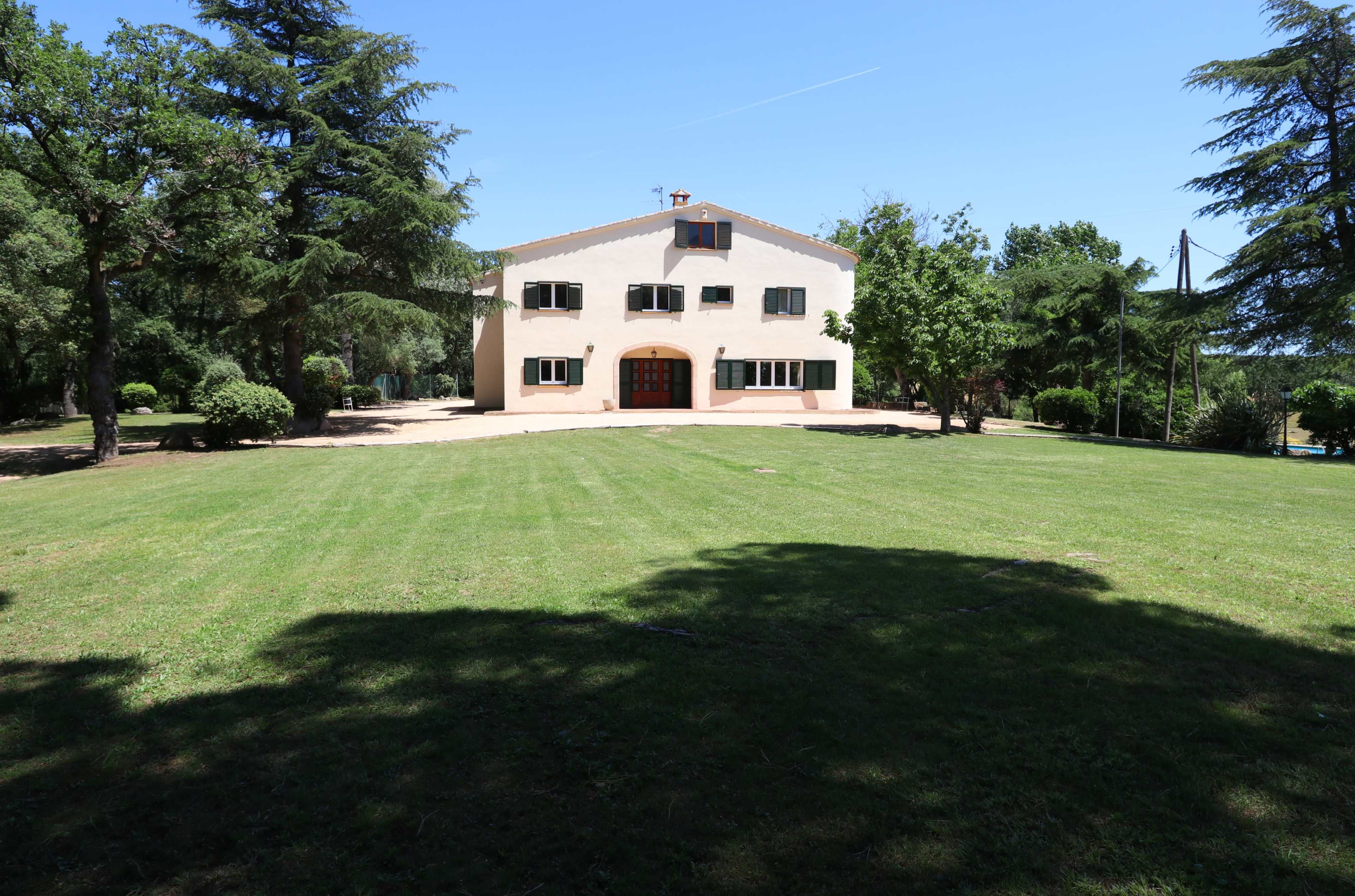 A large, two-story house with multiple windows stands in a grassy yard surrounded by tall trees.
