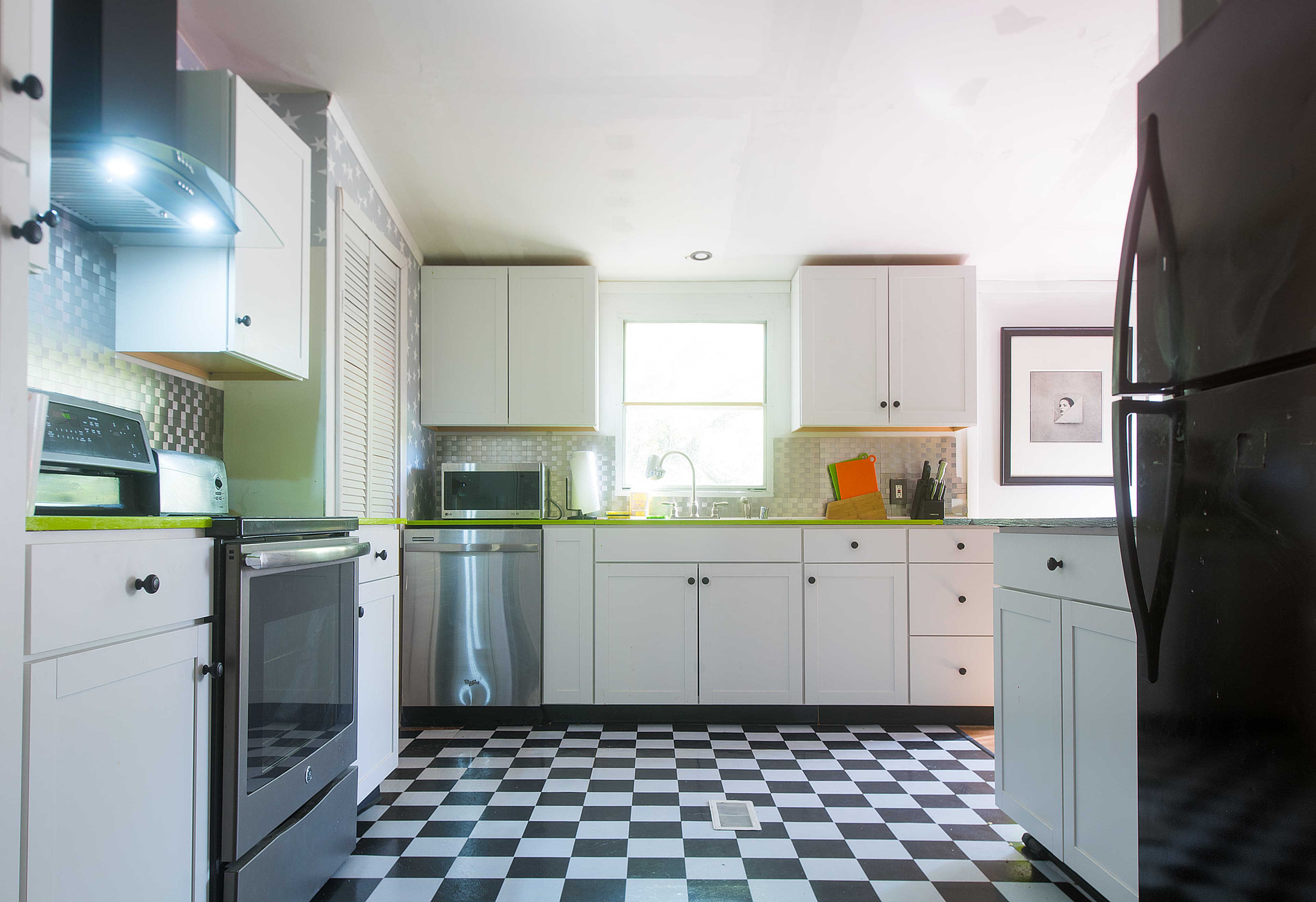 A modern kitchen with black and white checkered flooring, white cabinets, and stainless steel appliances.