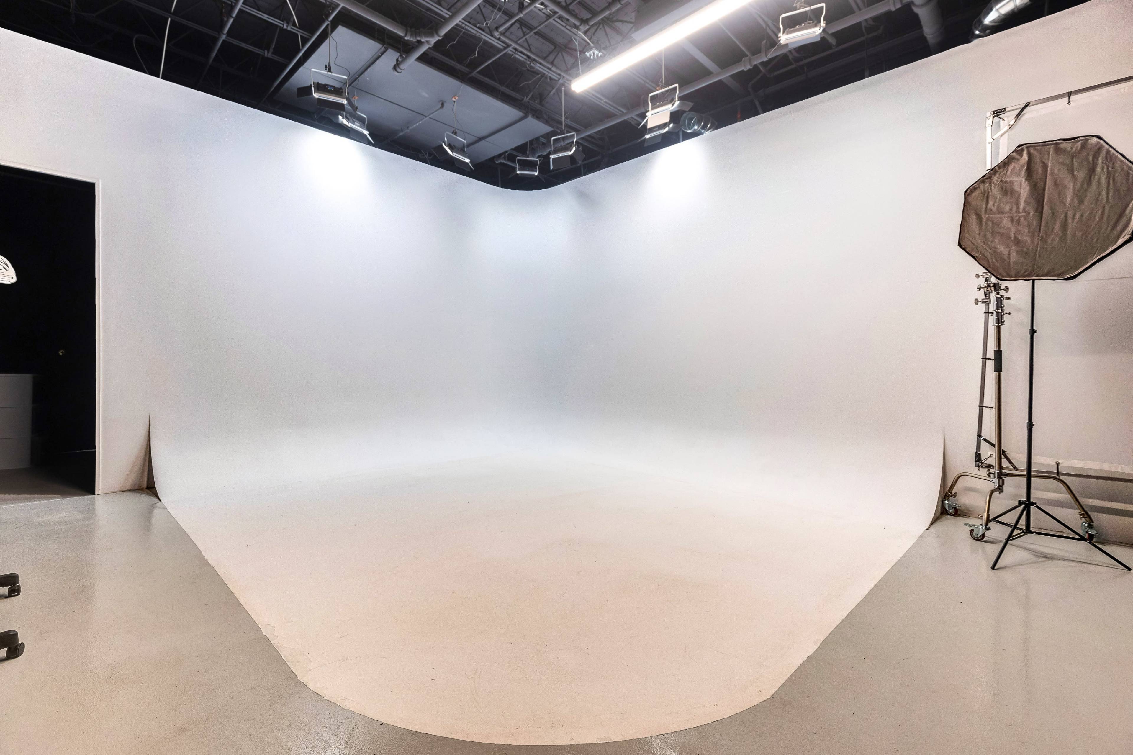 A large, empty photography studio with a seamless white backdrop and soft lighting equipment.