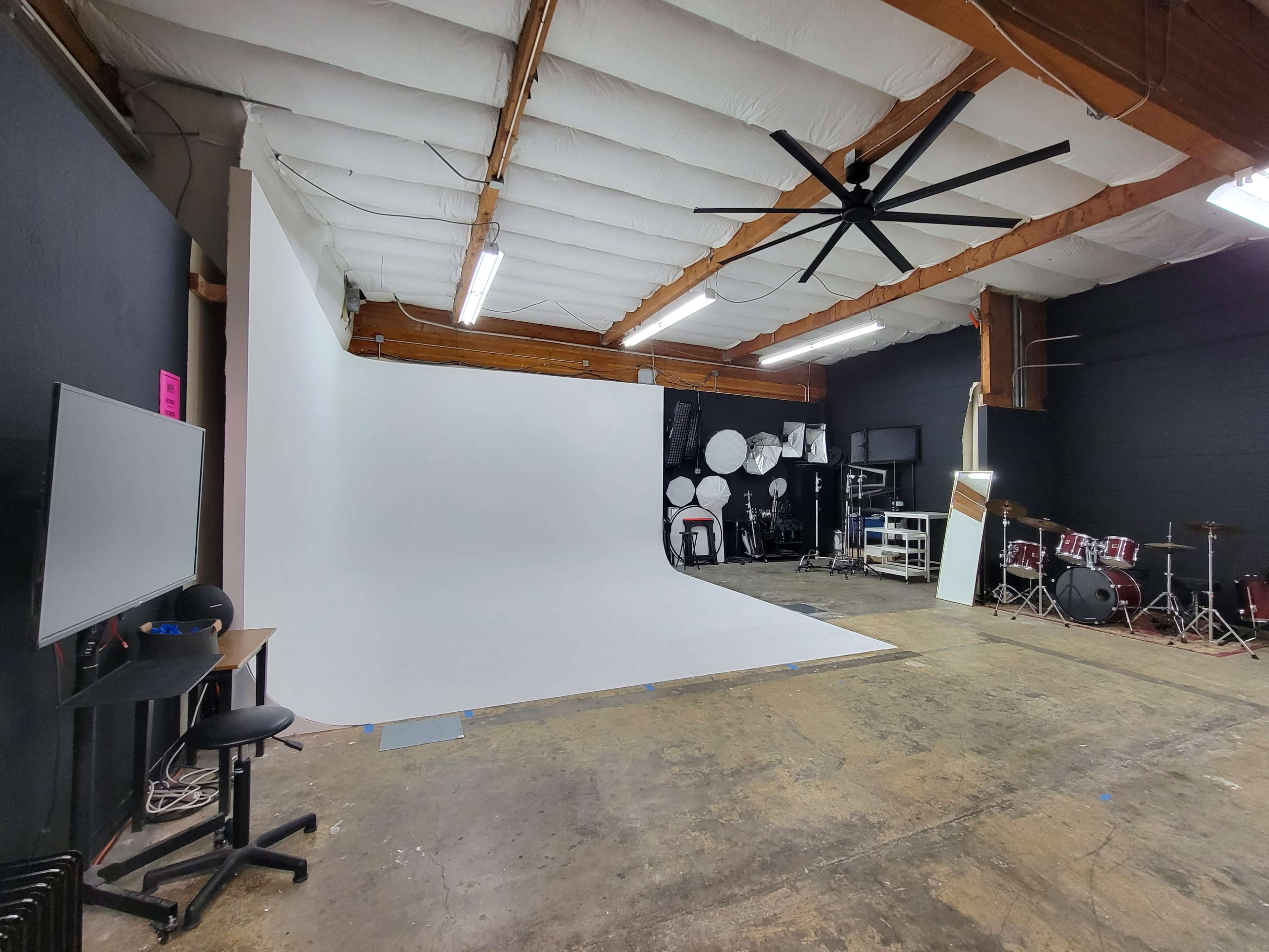 The image shows a spacious photography studio with a large white backdrop, various musical instruments in the background, and lighting fixtures.