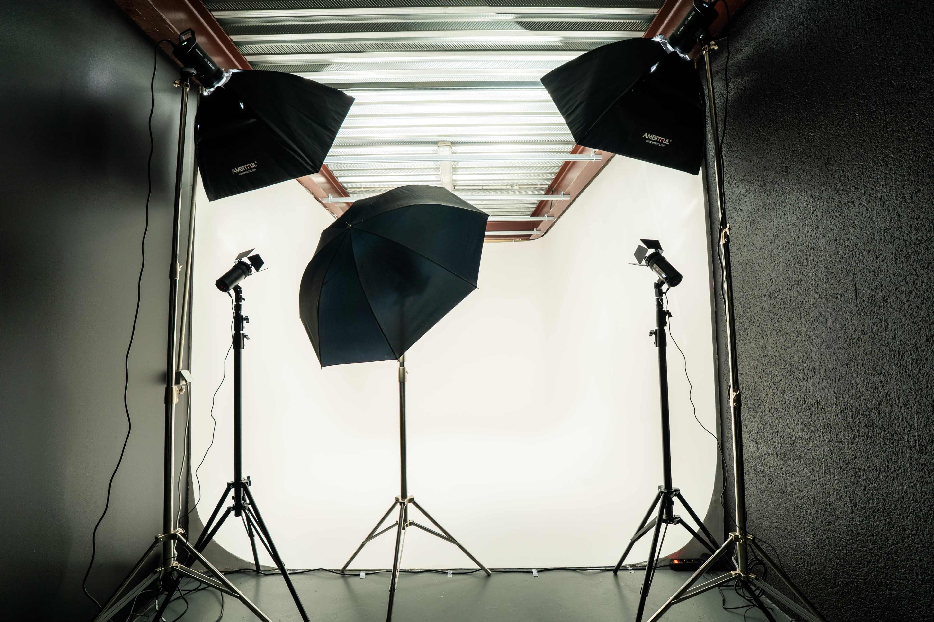 A photography studio is set up with three light stands and a white backdrop.