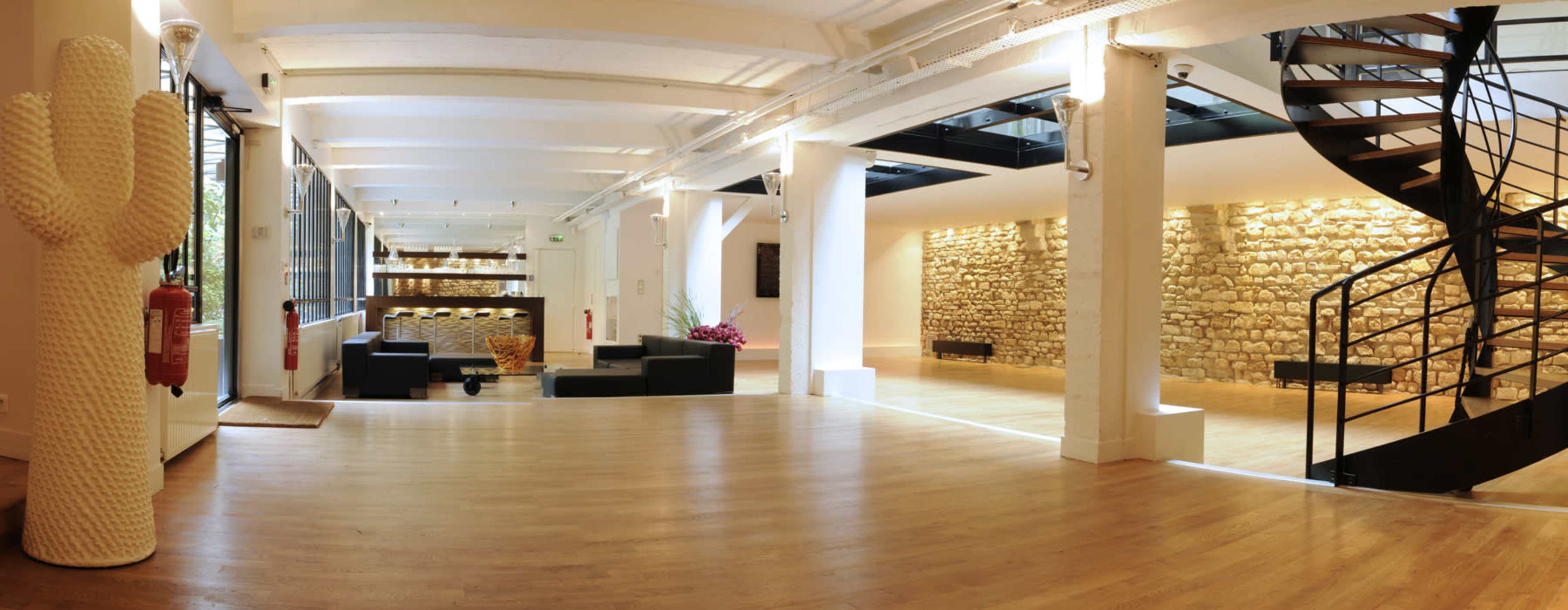 A spacious, modern interior with wooden floors, a sculptural cactus, and a spiral staircase leading to a bright, open area featuring stone walls.