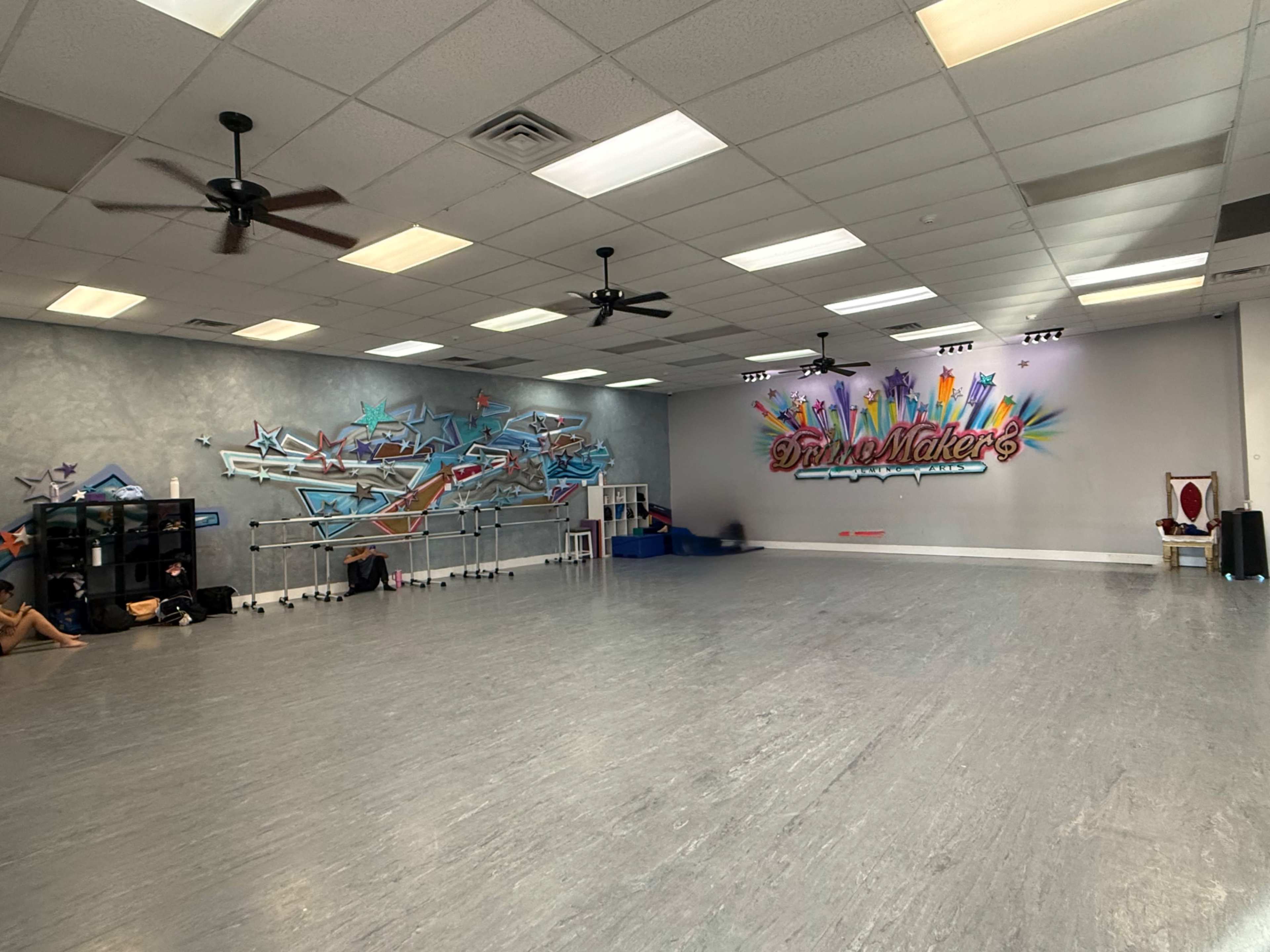 The image shows an empty dance studio with two walls featuring colorful graffiti art and a spacious wooden floor.