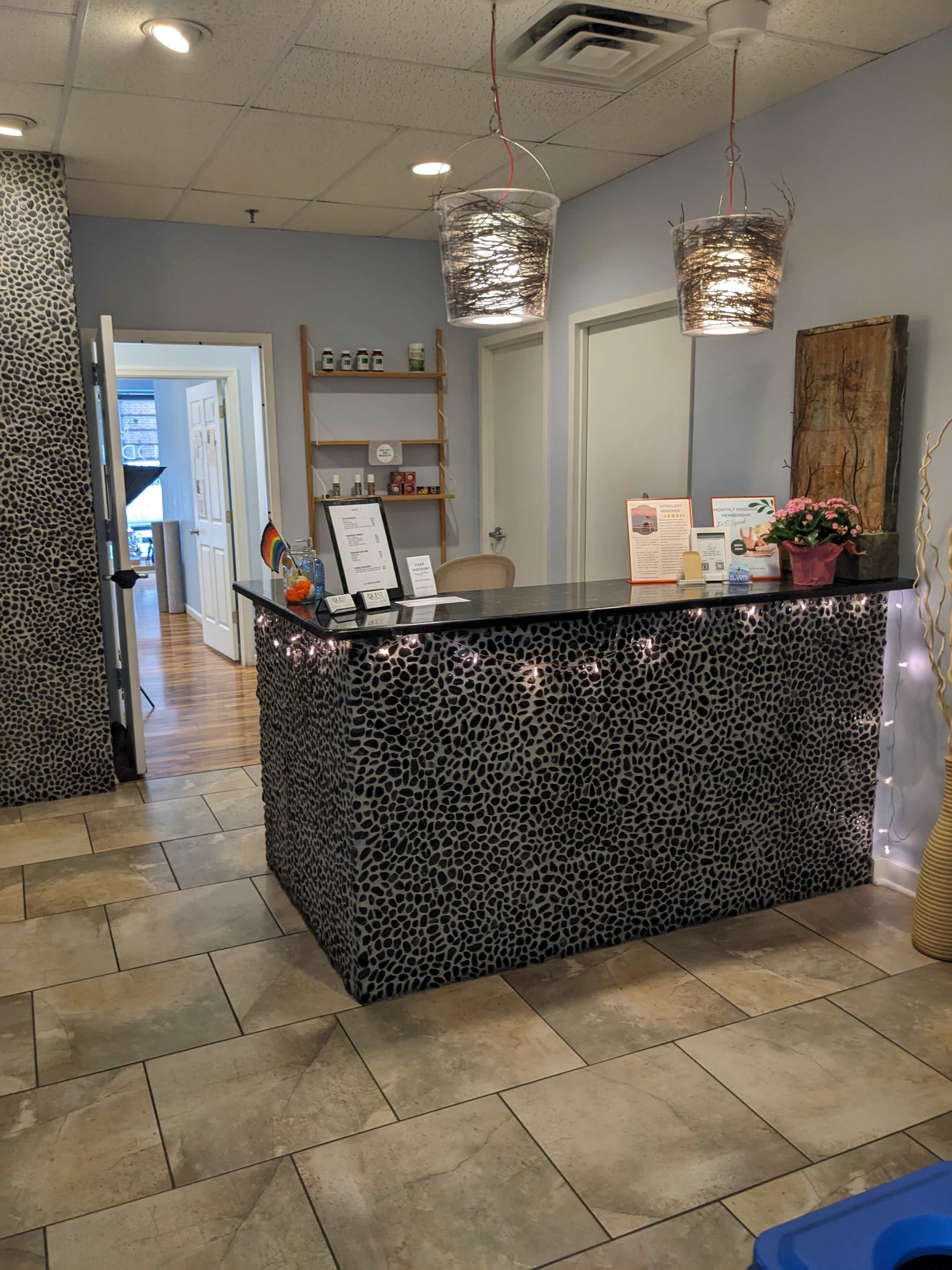 The image shows a reception area featuring a patterned stone front desk, two hanging light fixtures, and an entrance leading to another room.