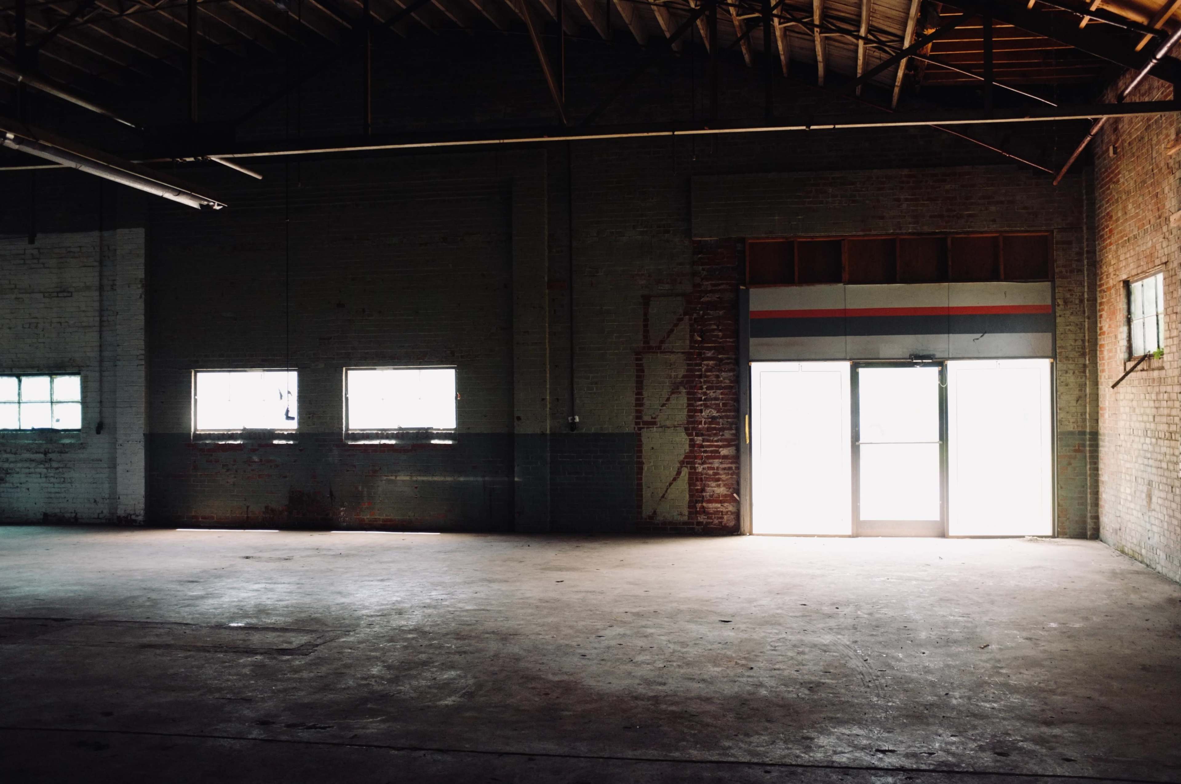 The image shows an empty industrial space with a concrete floor and large windows letting in natural light.