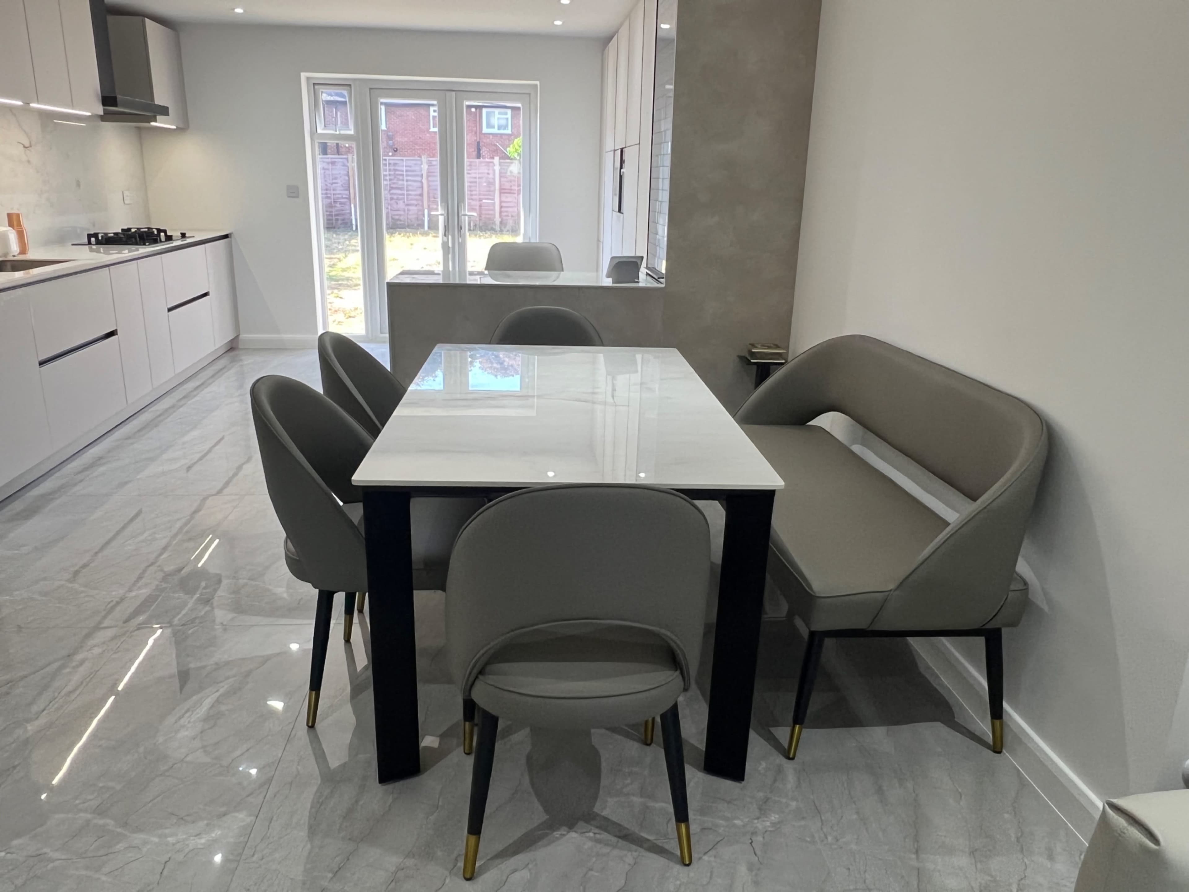 A modern kitchen features a marble dining table surrounded by four upholstered chairs with a light-colored interior.
