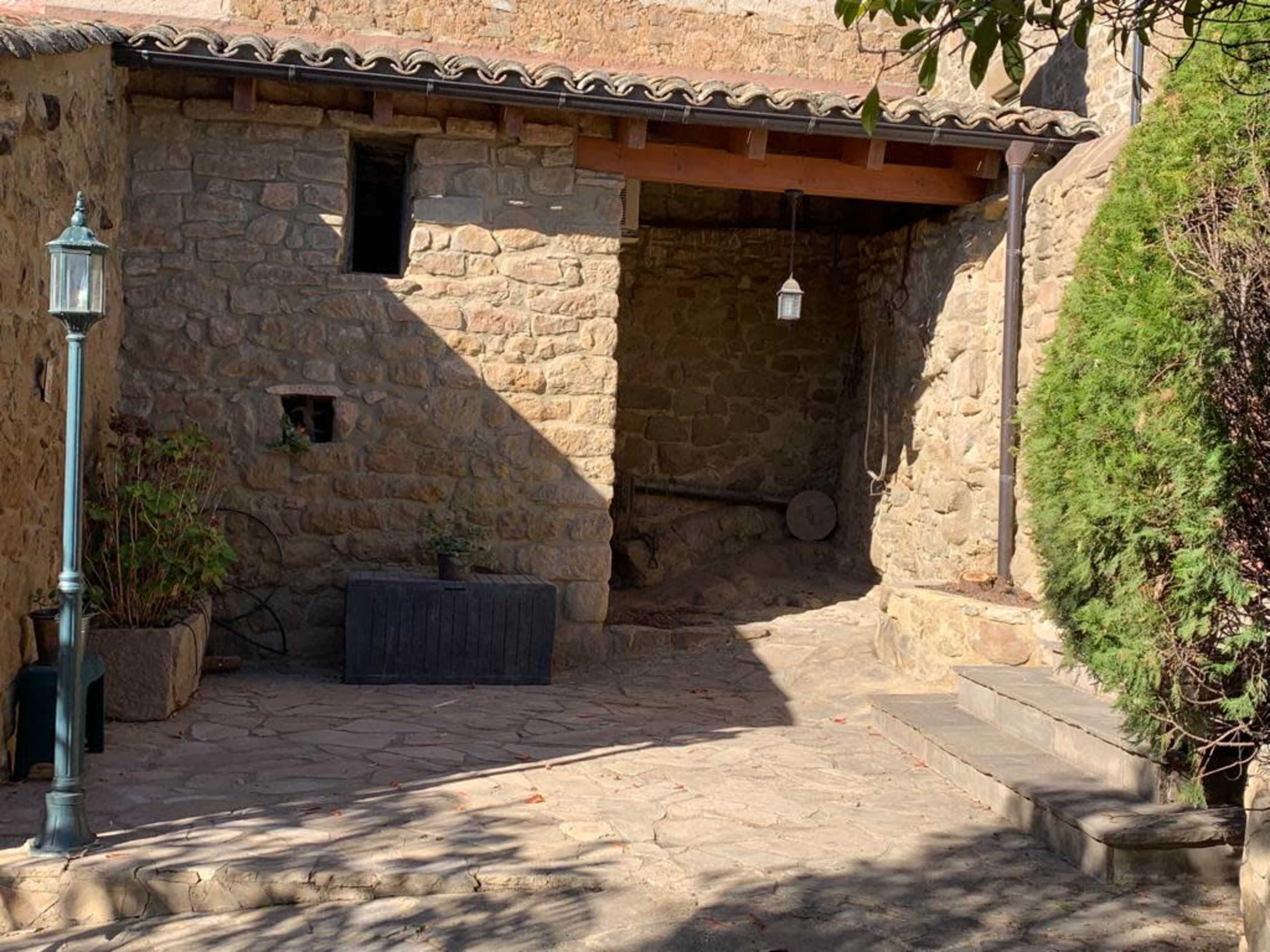 The image shows a stone-walled patio area with a lantern, a planter, and steps leading to a shaded corner.