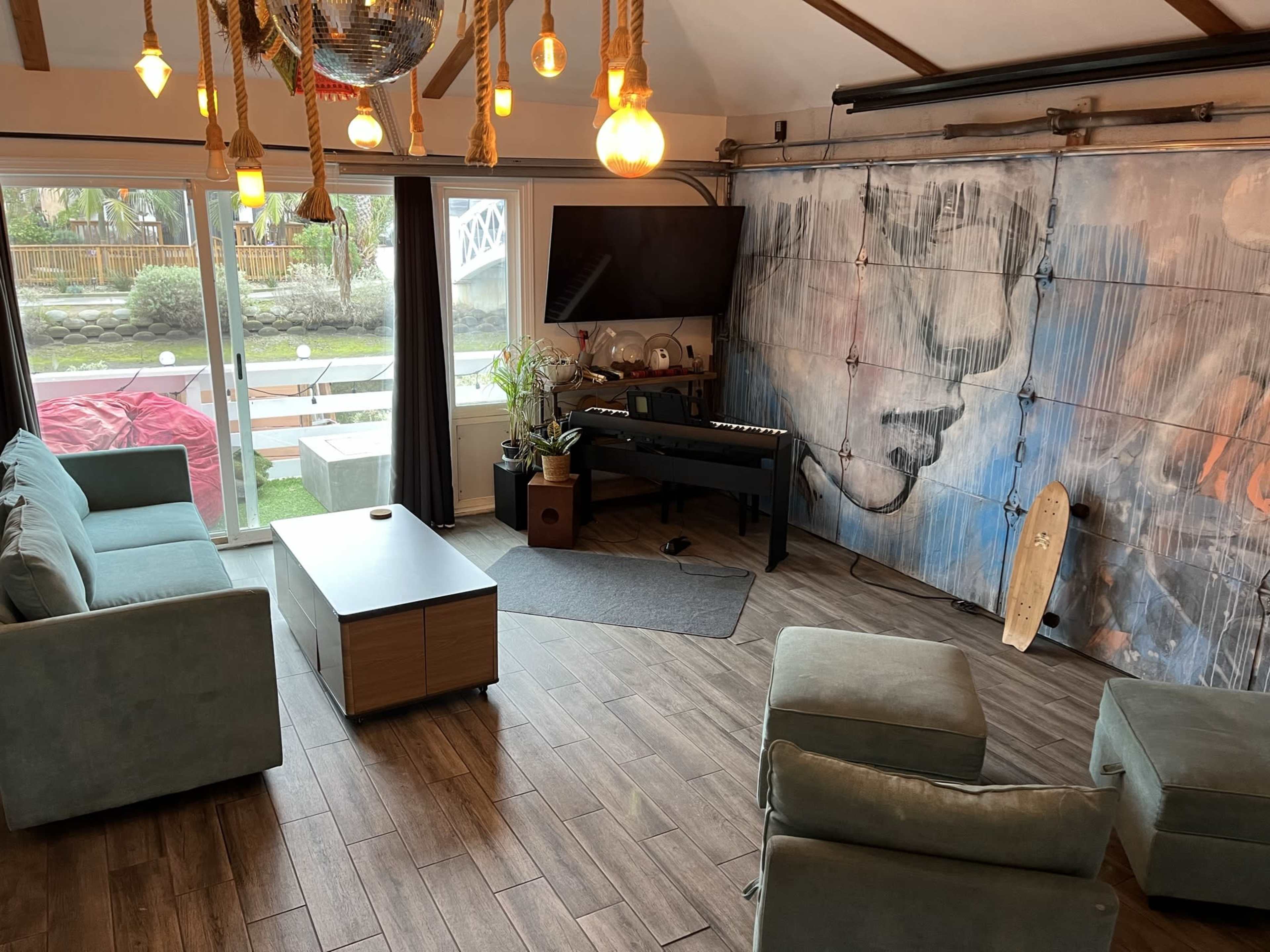 A modern living space with a large window, a television mounted on the wall, a piano, and a colorful mural.