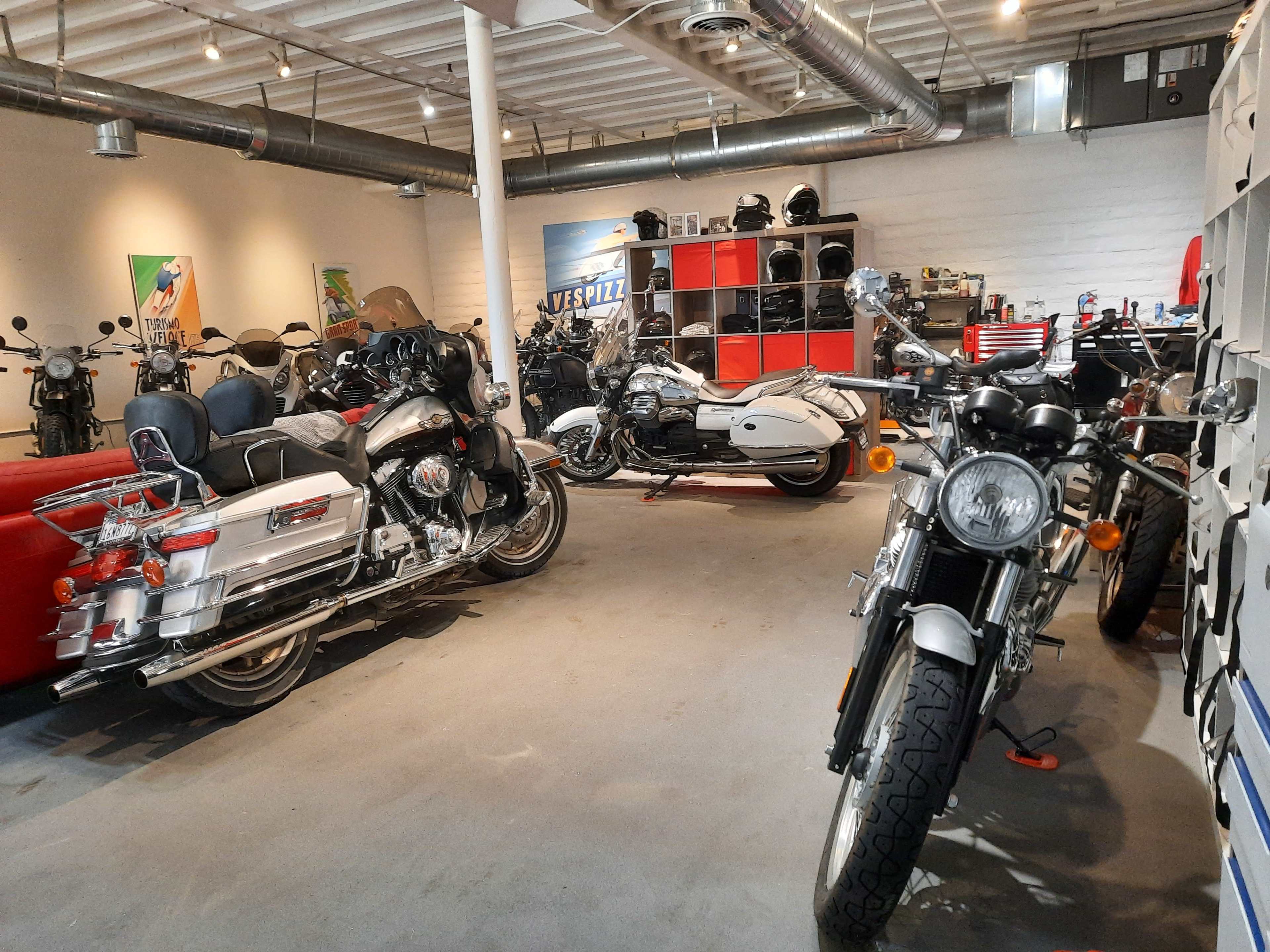 A spacious motorcycle garage featuring several parked motorcycles and various tools and equipment organized in the background.