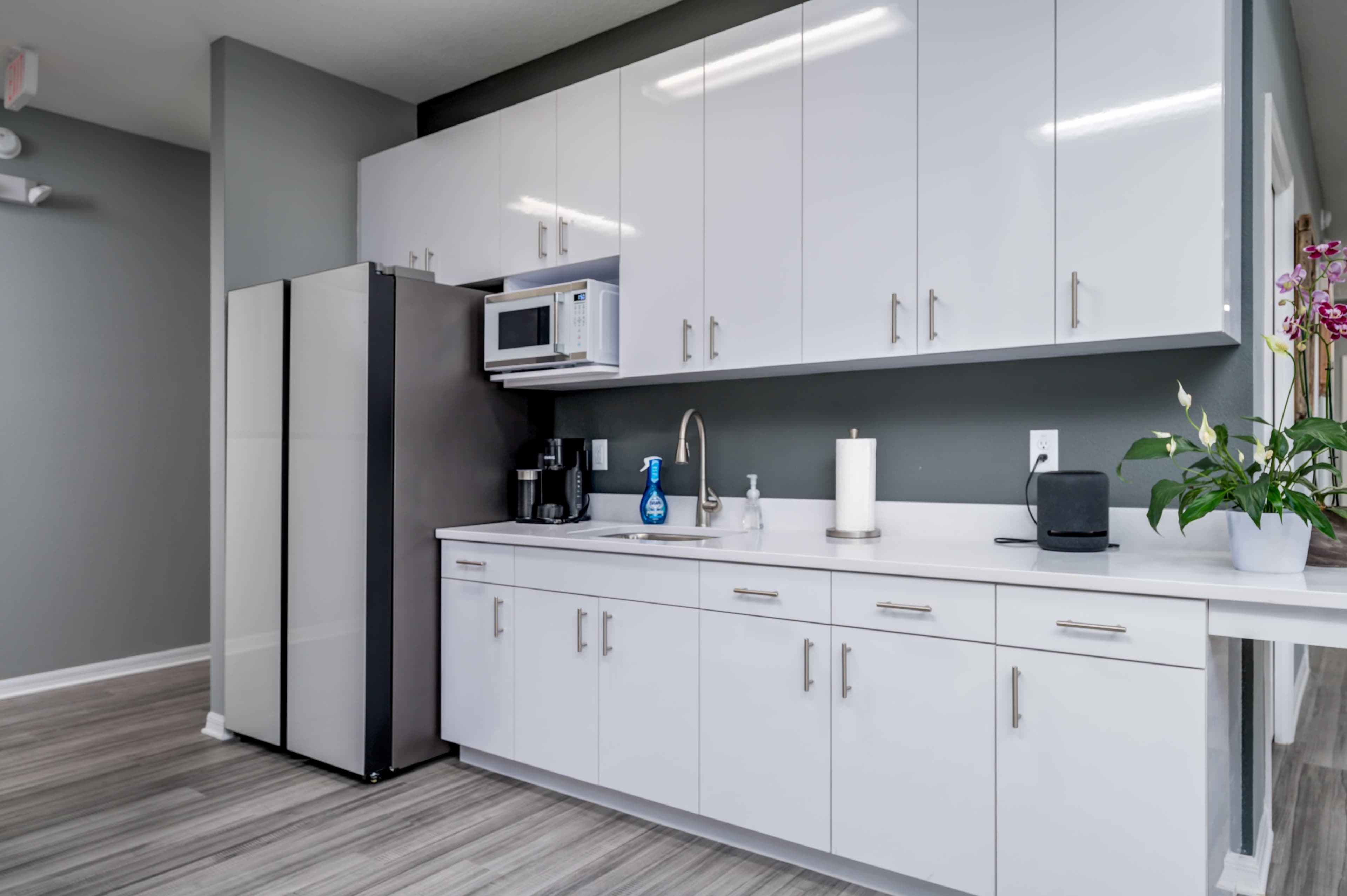 A modern kitchen with white cabinetry, a refrigerator, a microwave, and a coffee maker on the countertop.