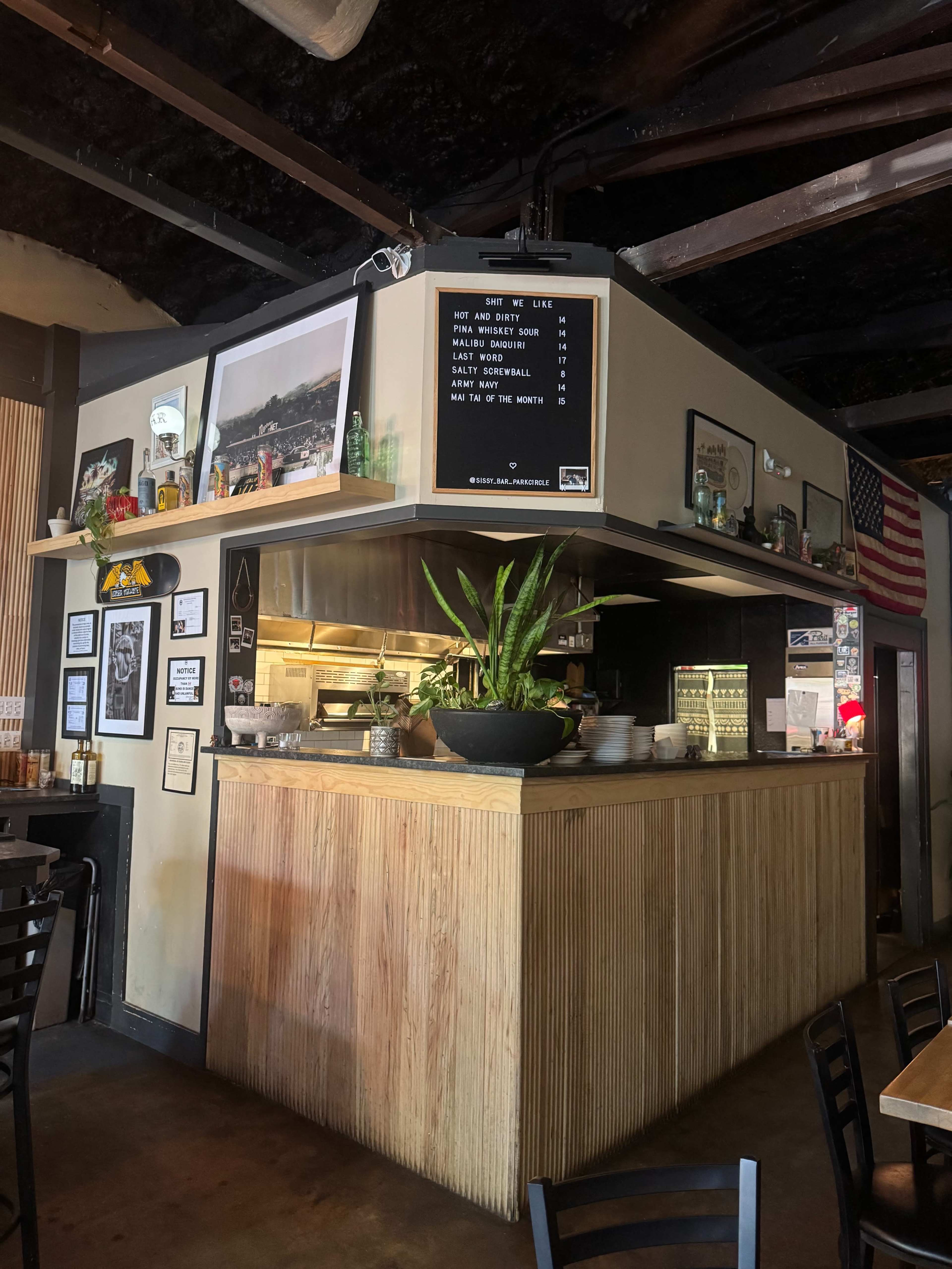 The image shows a cozy restaurant interior with a wooden service counter, framed photographs on the walls, and an American flag hanging above.
