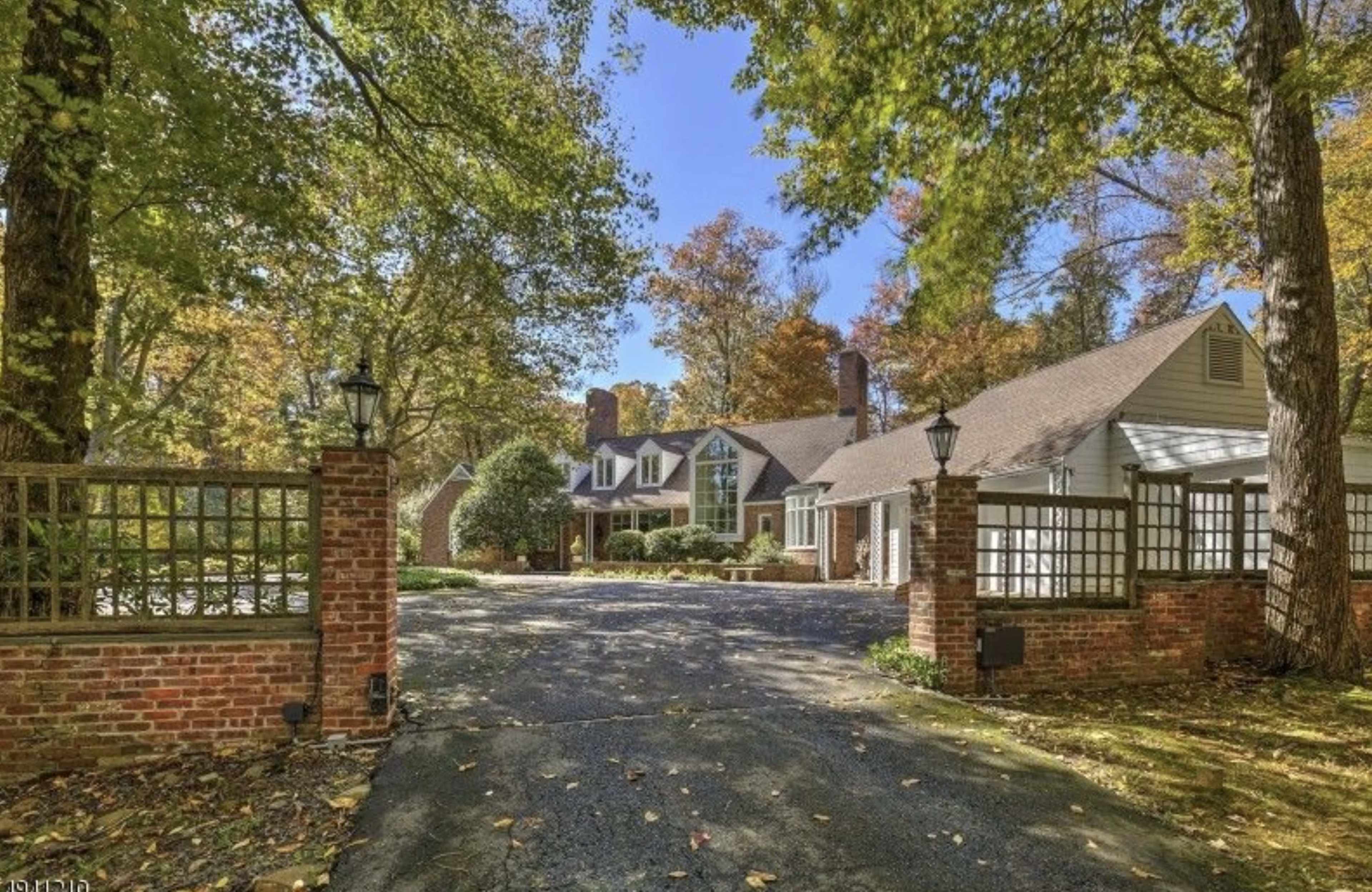 A large, traditional-style home set back from a tree-lined driveway surrounded by autumn foliage.