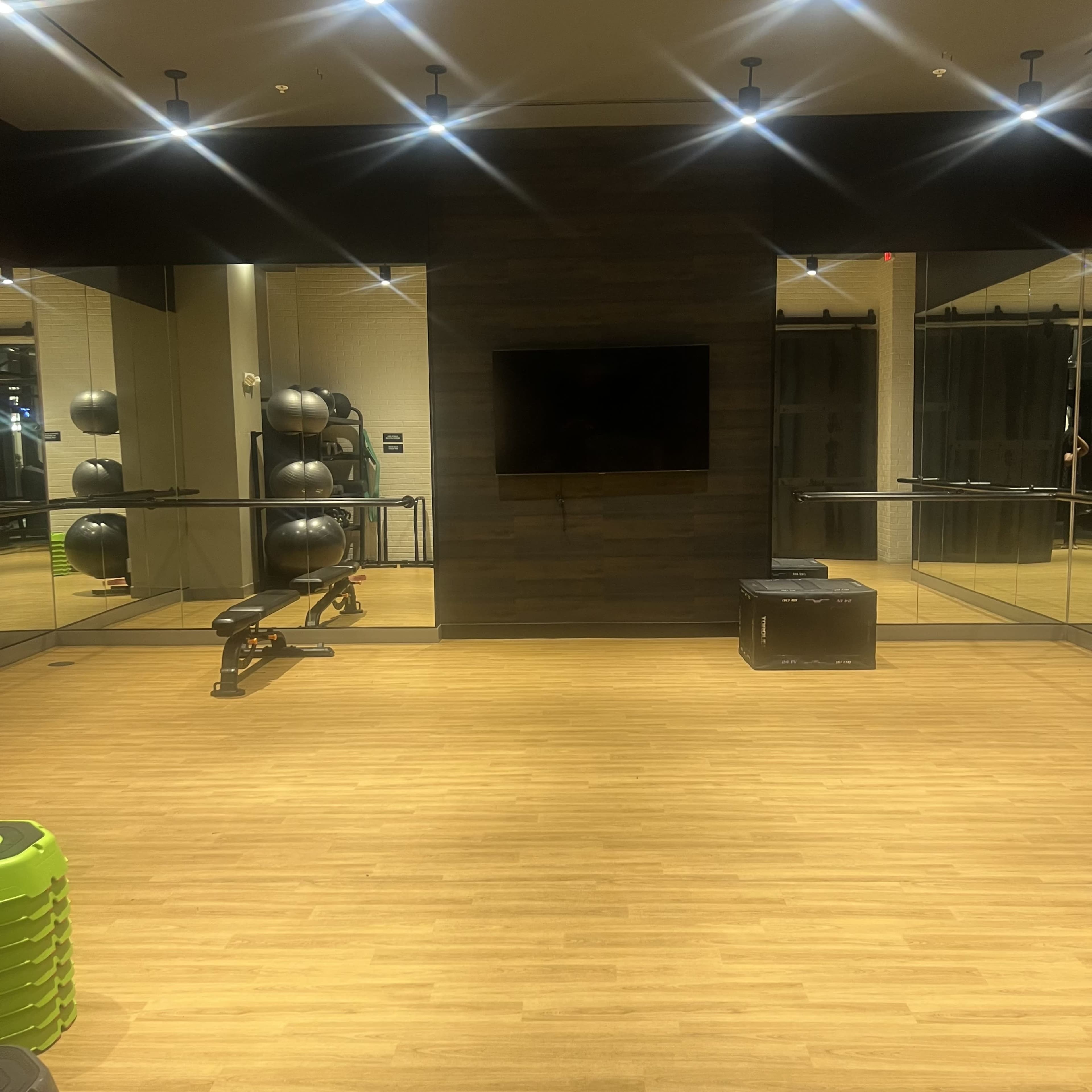 The image shows a minimalist gym space with a workout bench, a television mounted on the wall, and exercise balls arranged in the background.