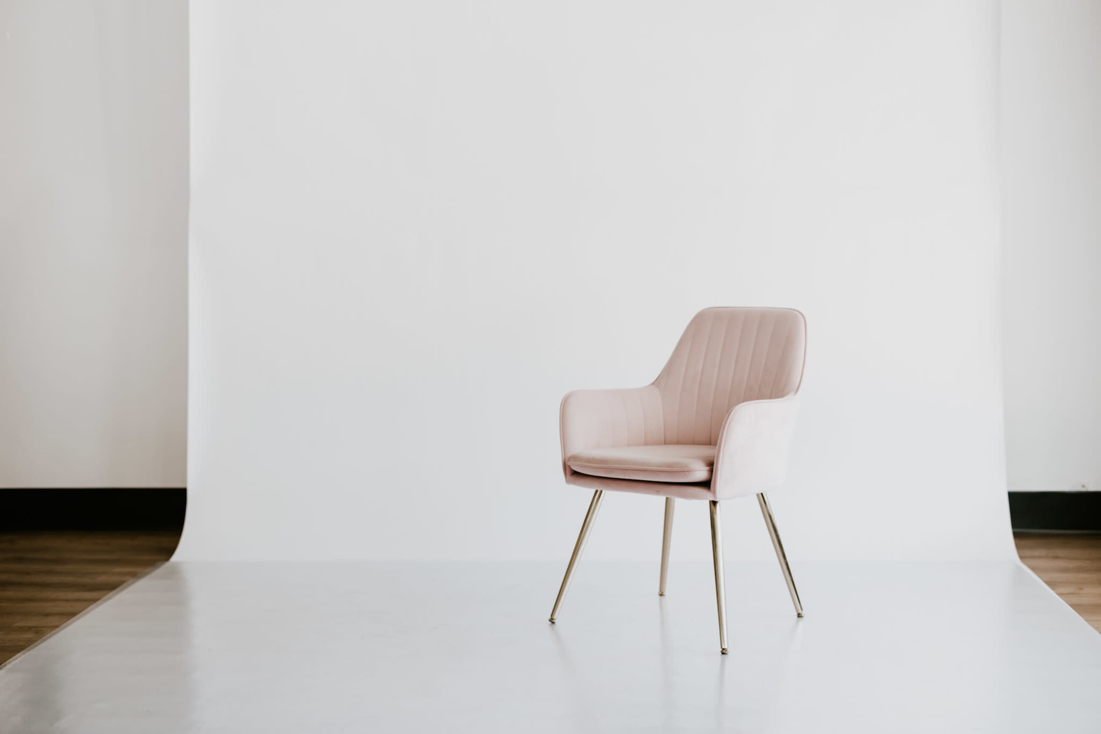 A pink upholstered chair with metallic legs is positioned in front of a white backdrop.