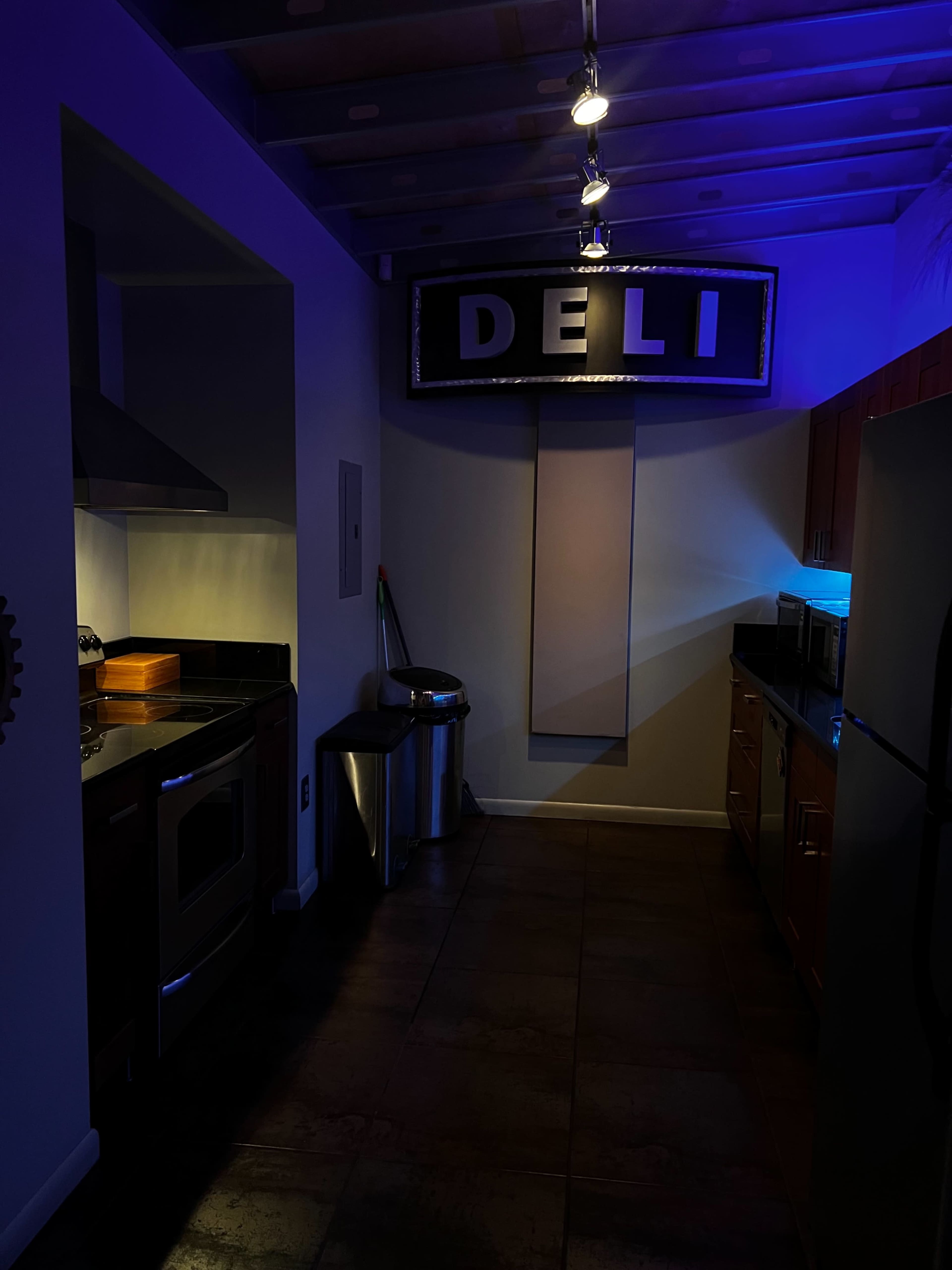 A dimly lit kitchen area with a "DELI" sign hanging above and modern appliances on the counters.