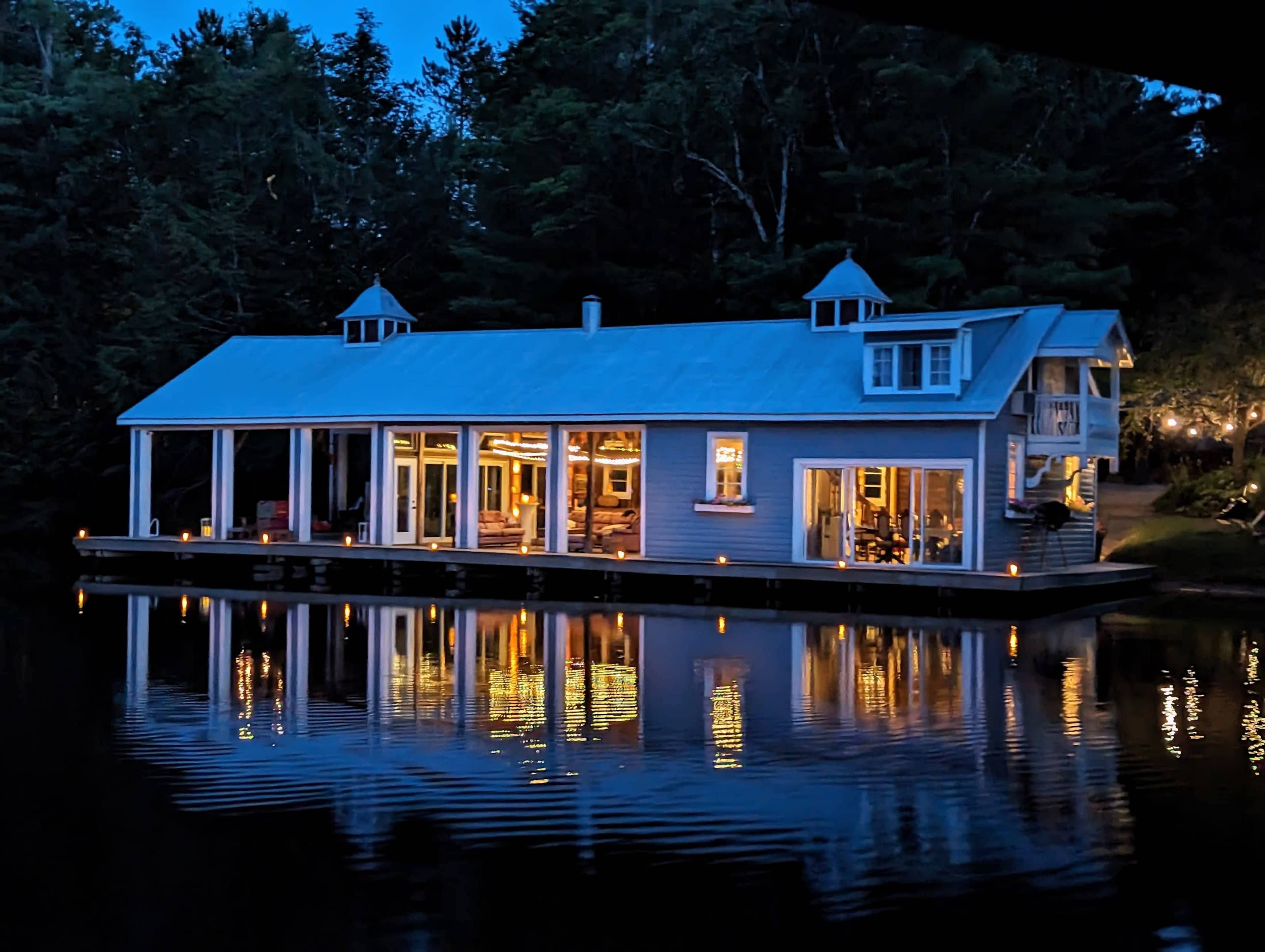 A lakeside house with large windows and a dock reflects in the calm water at dusk.
