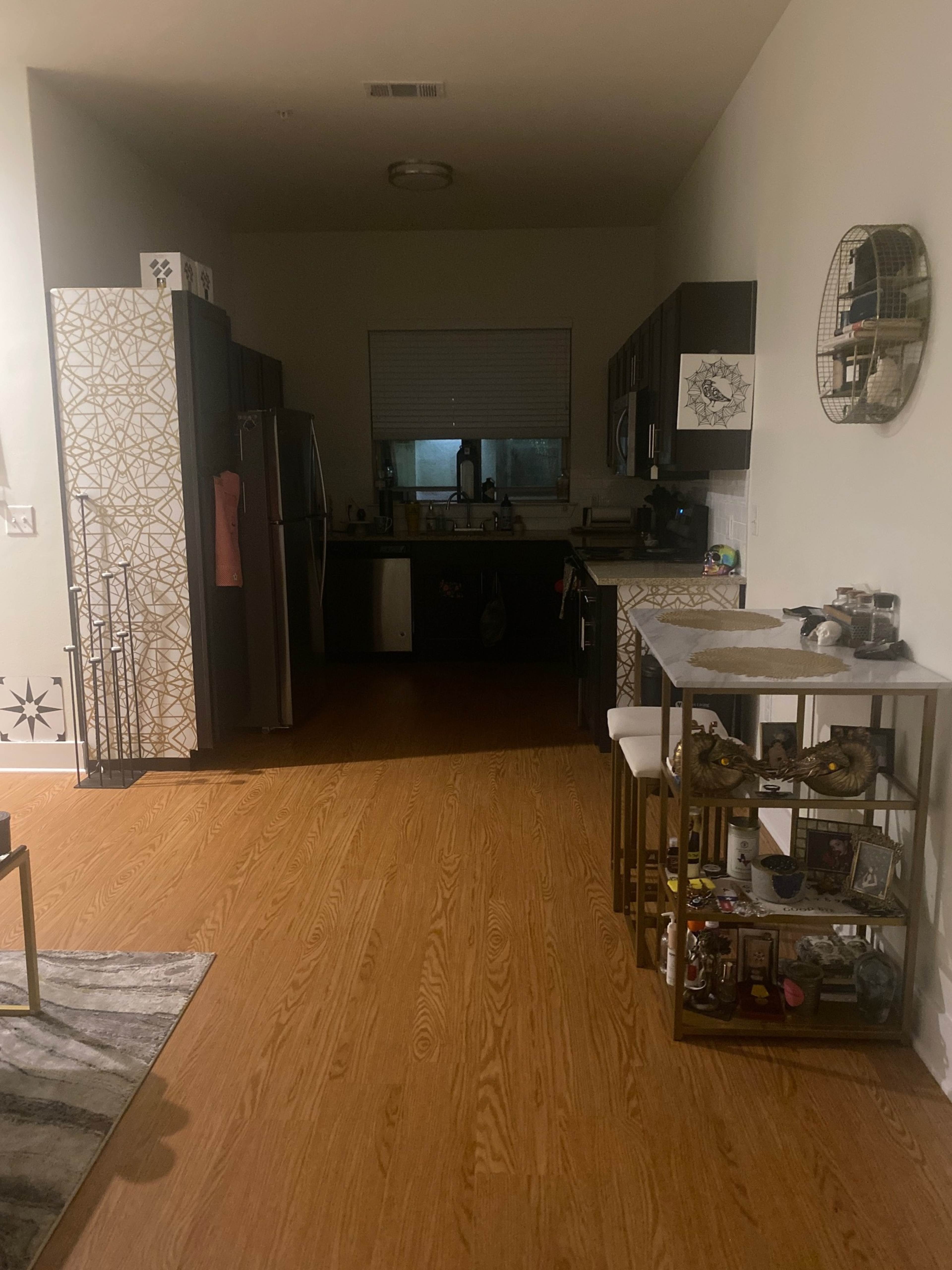 The image shows a dimly lit kitchen with dark cabinets, a stainless steel refrigerator, and a small dining table at the forefront.
