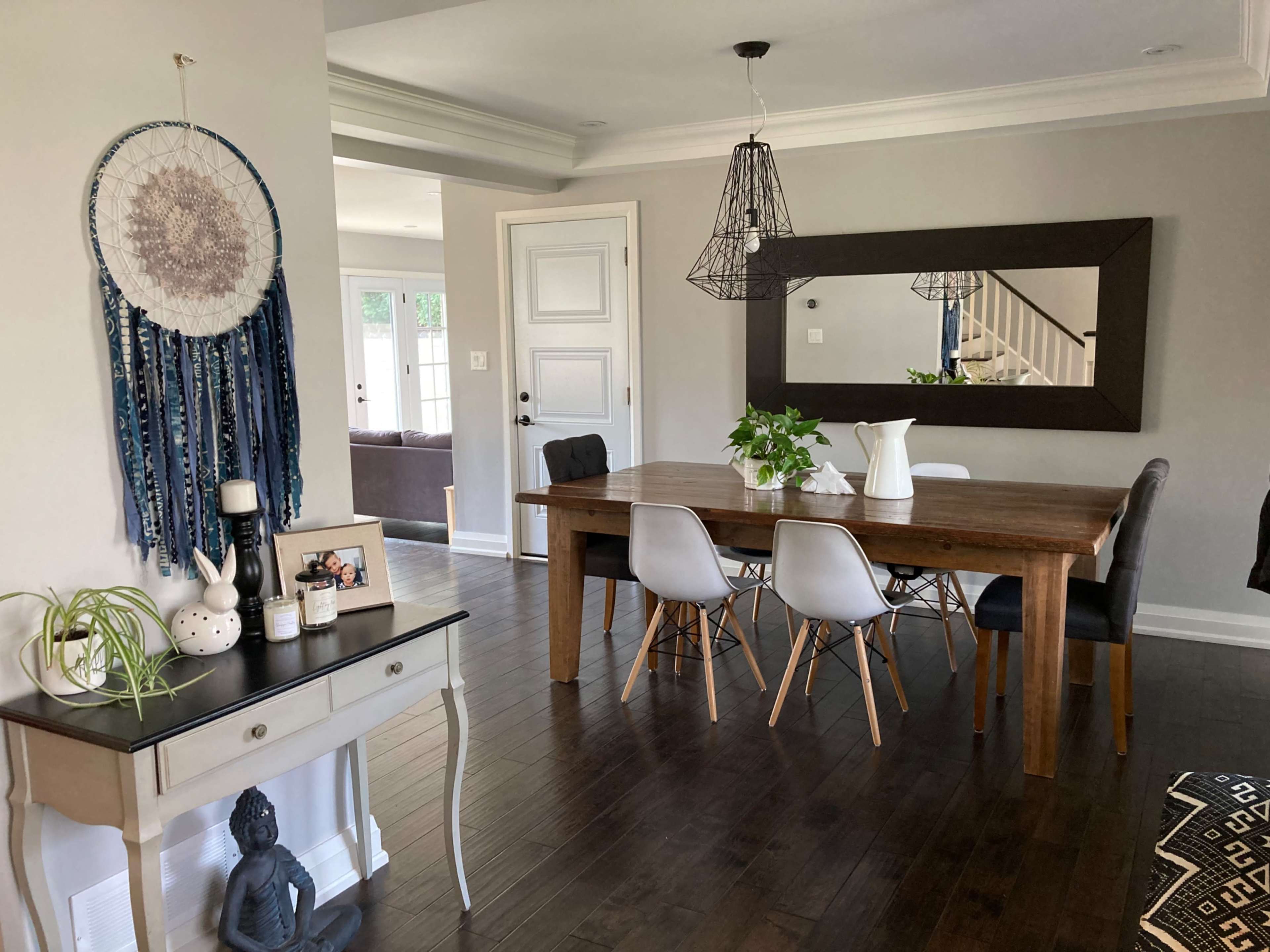 A modern dining area featuring a wooden table surrounded by chairs, a large mirror on the wall, and decorative elements including a plant and art pieces.