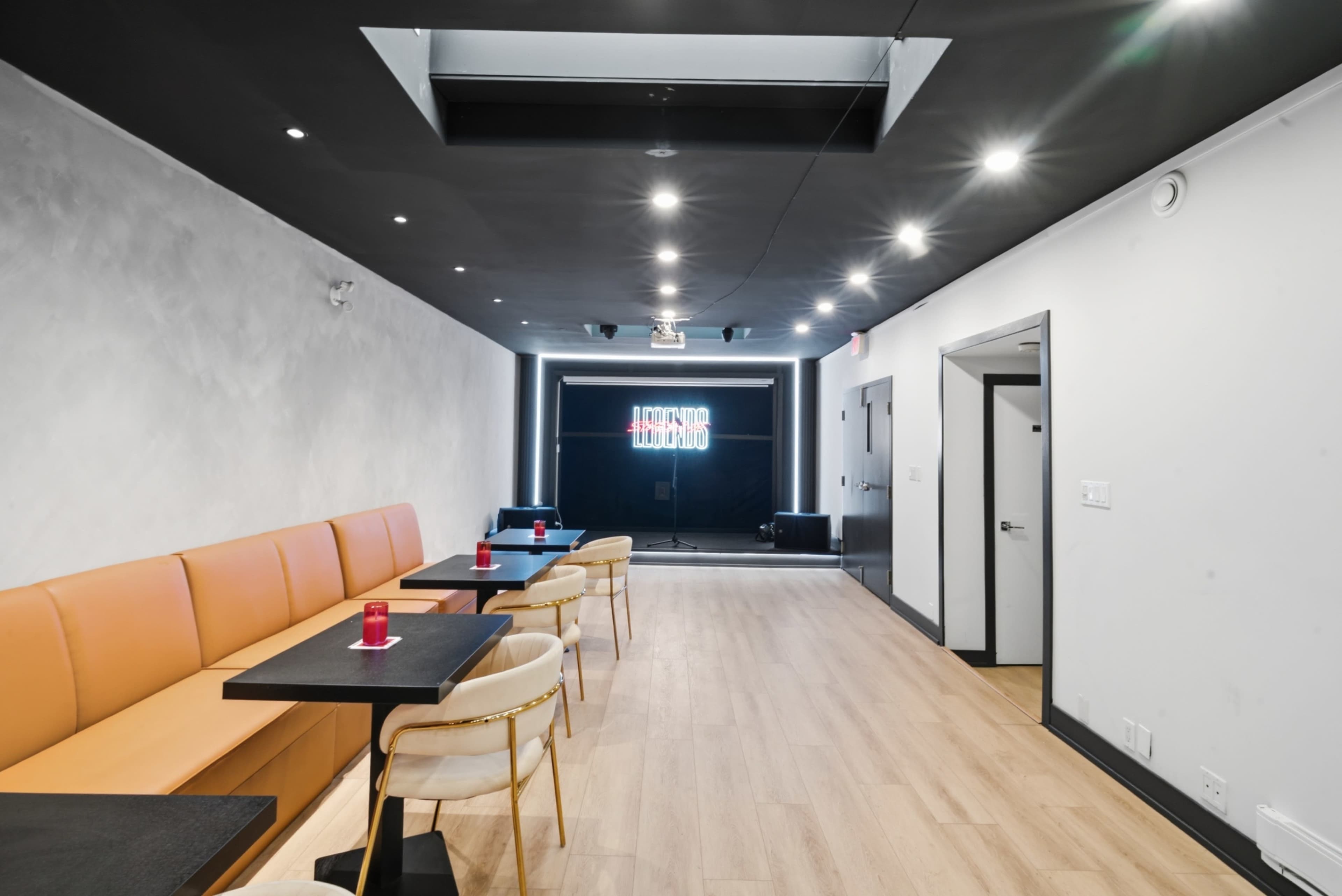 The image shows a modern interior of a stylish lounge with orange seating, black tables, and ambient lighting.