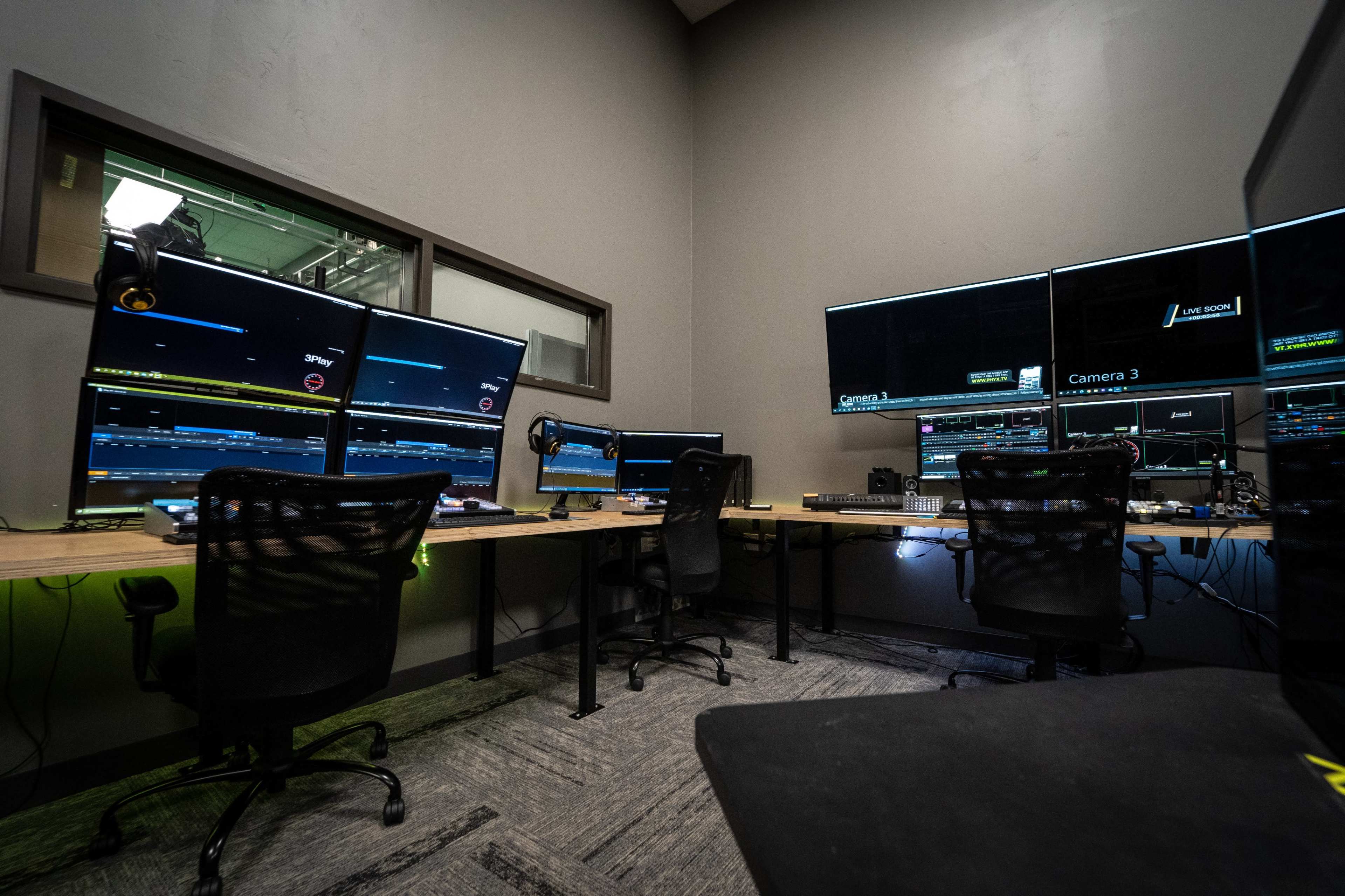 The image shows a modern control room equipped with multiple computer monitors, each displaying various camera feeds and data, alongside three office chairs.