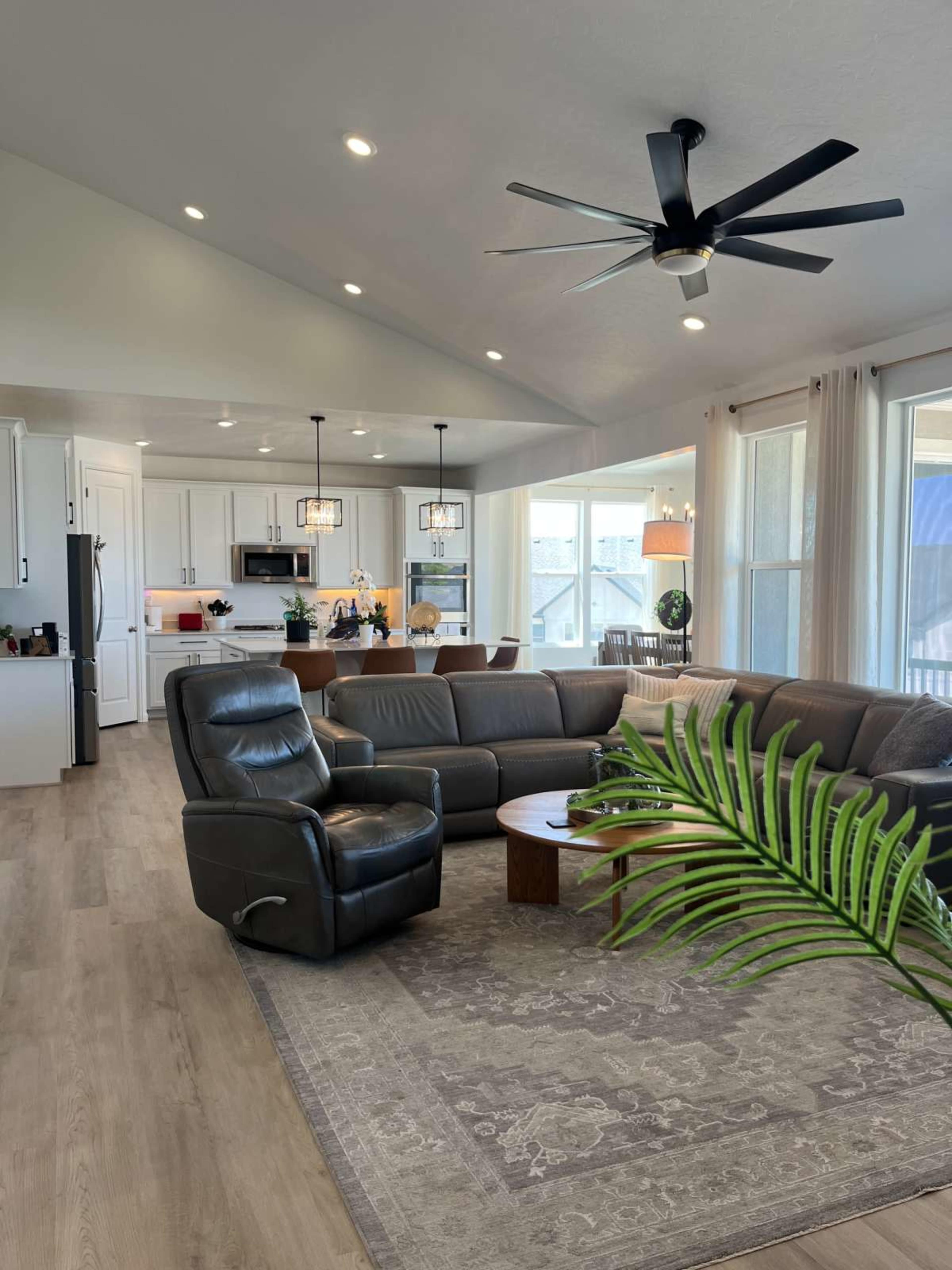 The image shows a modern living room with a large sectional sofa, a coffee table, and a kitchen area in the background.