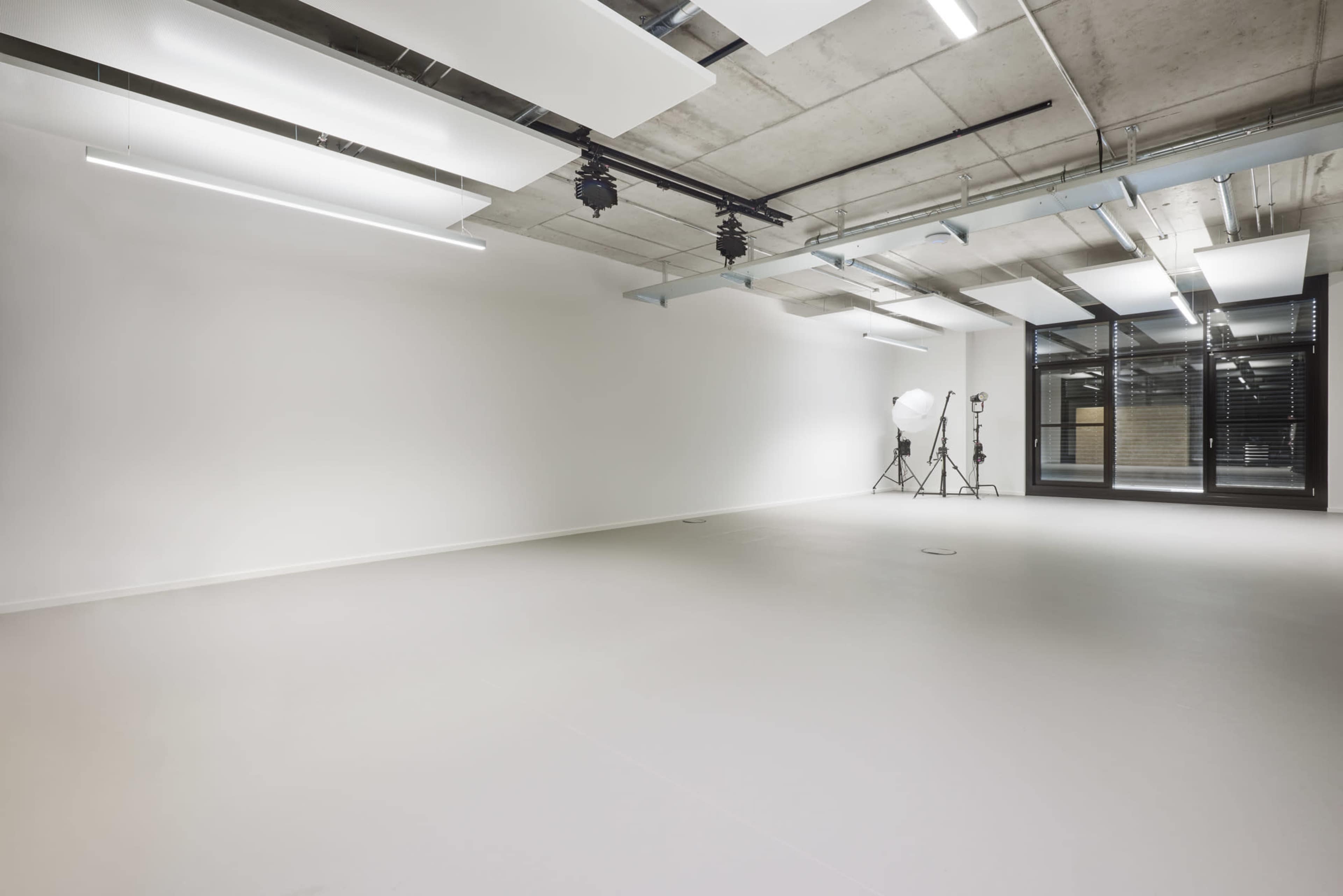 A spacious, empty room with concrete walls, industrial lighting, and photography equipment in the corner.