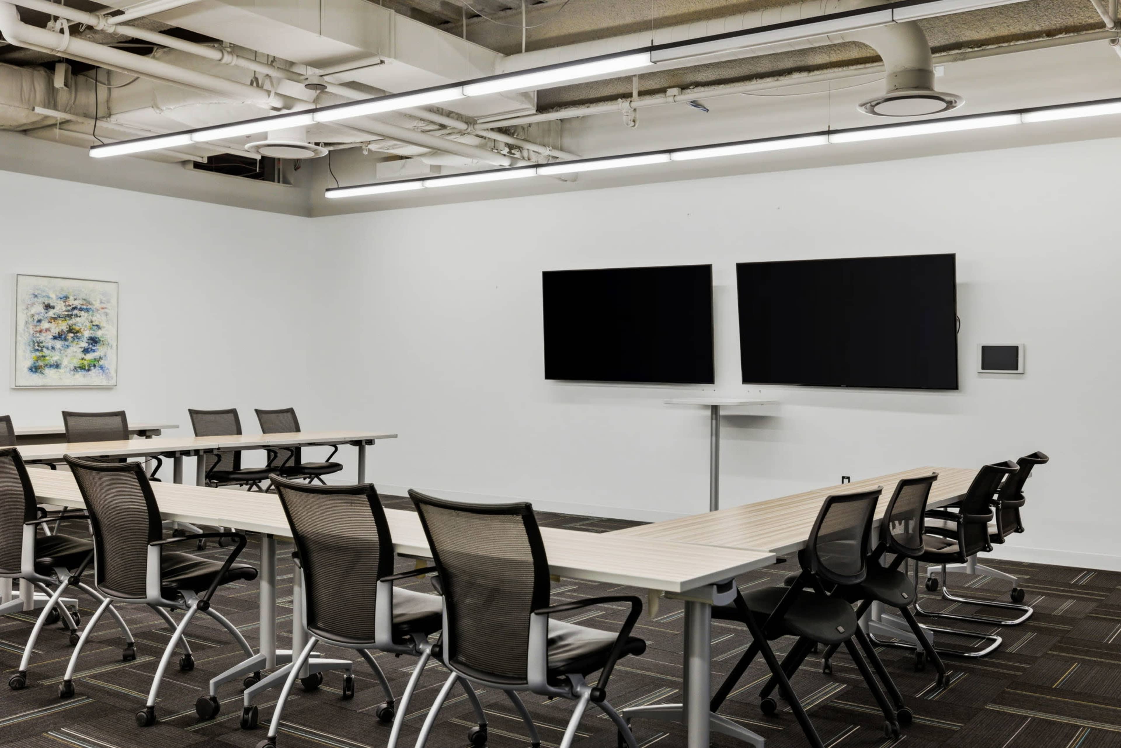 A modern conference room features two large screens, several long tables, and ergonomic chairs arranged for meetings.