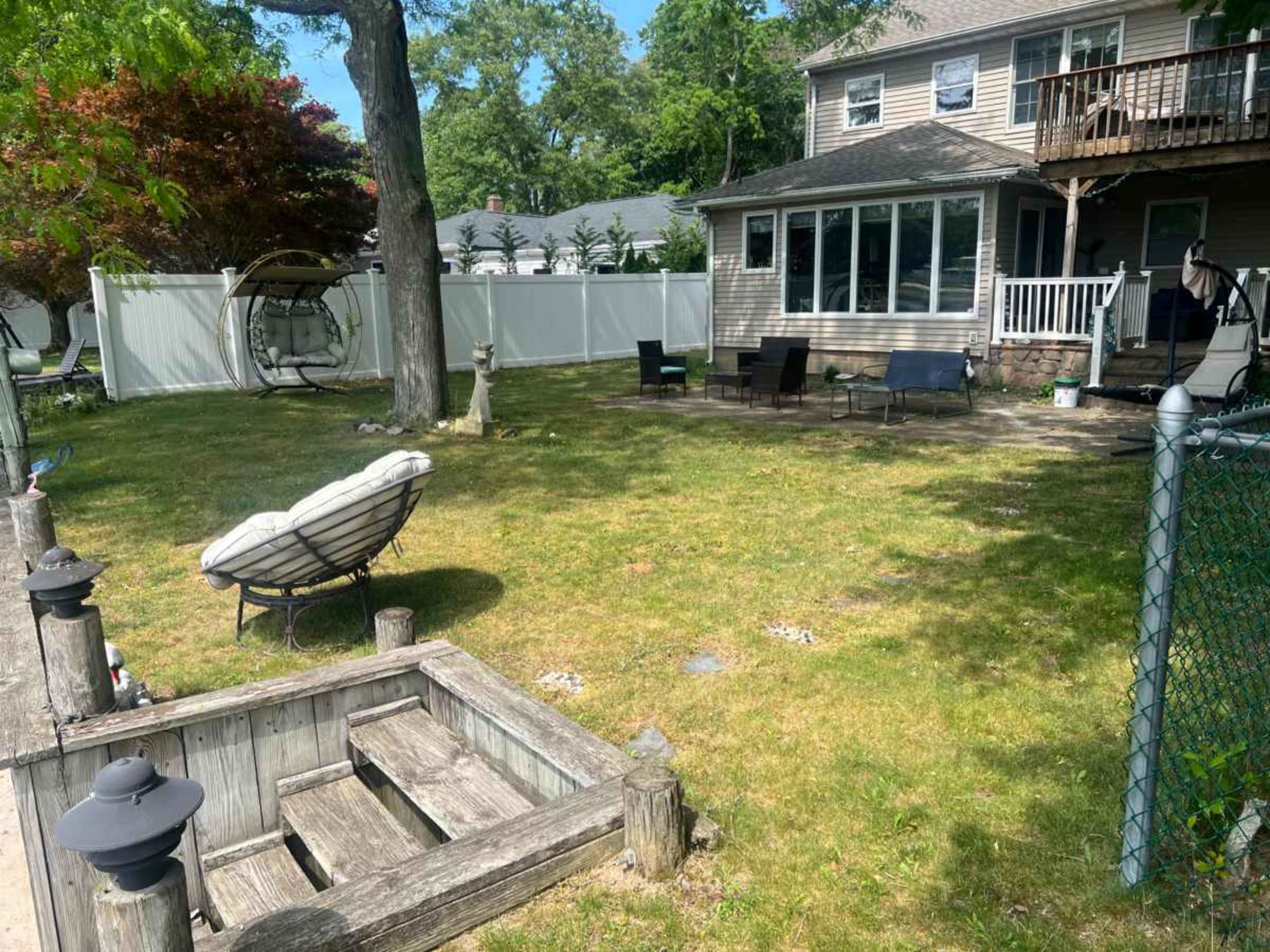 The image shows a backyard with a grassy area, a swing chair, several lounge chairs, and a house with a deck in the background.