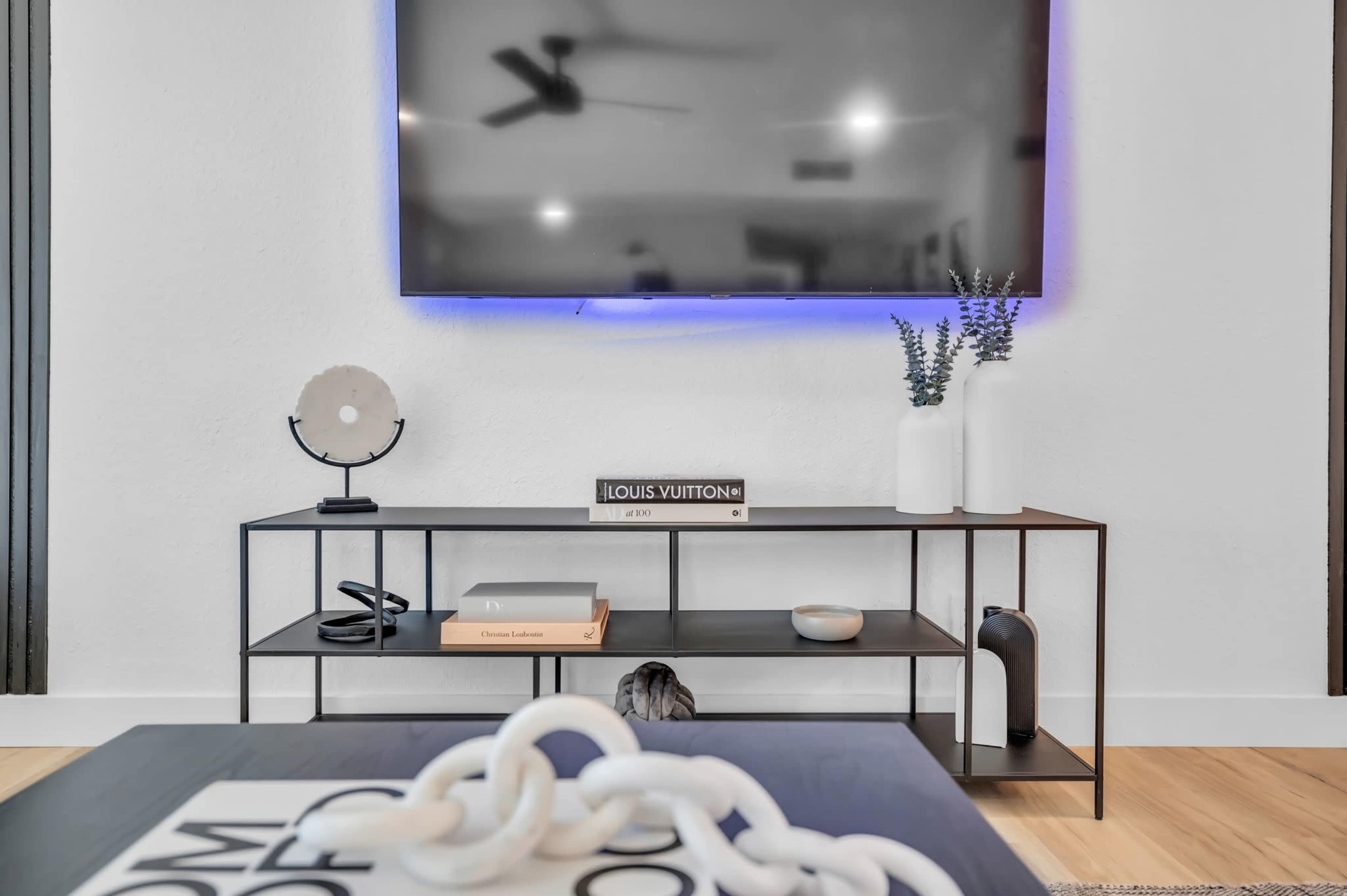 A modern living room features a sleek TV mounted on the wall above a black metal media console with decorative items and books.