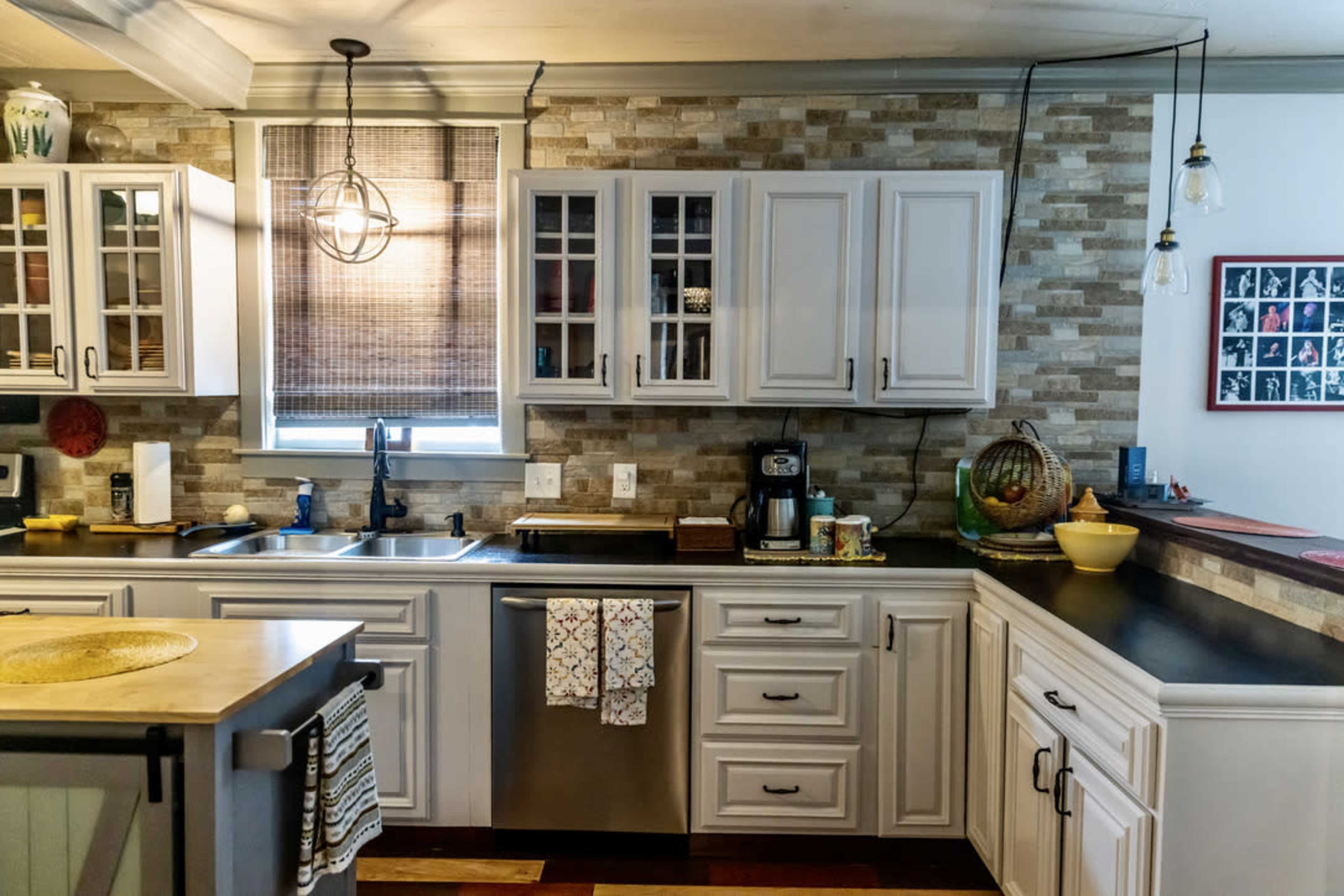 A modern kitchen with white cabinetry, a stainless steel sink, and an island, featuring a mix of stone and wooden elements.