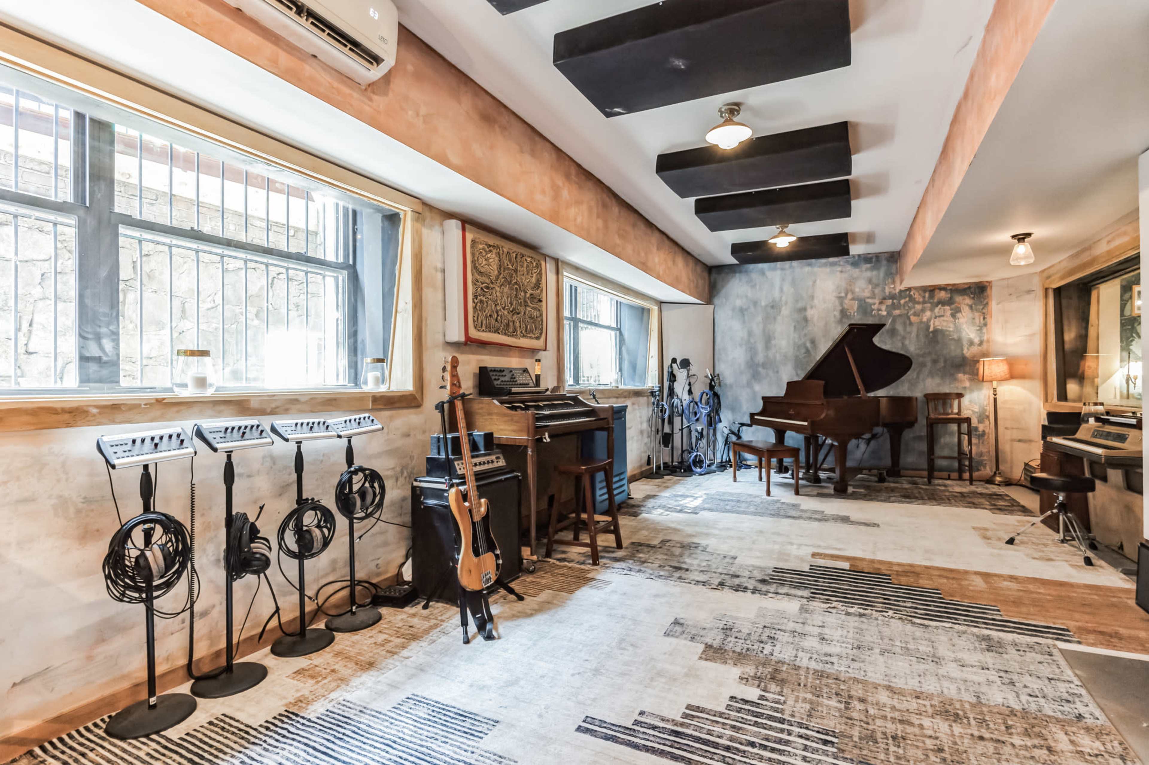 A music studio with a grand piano, various instruments on stands, and soundproofing panels on the ceiling.
